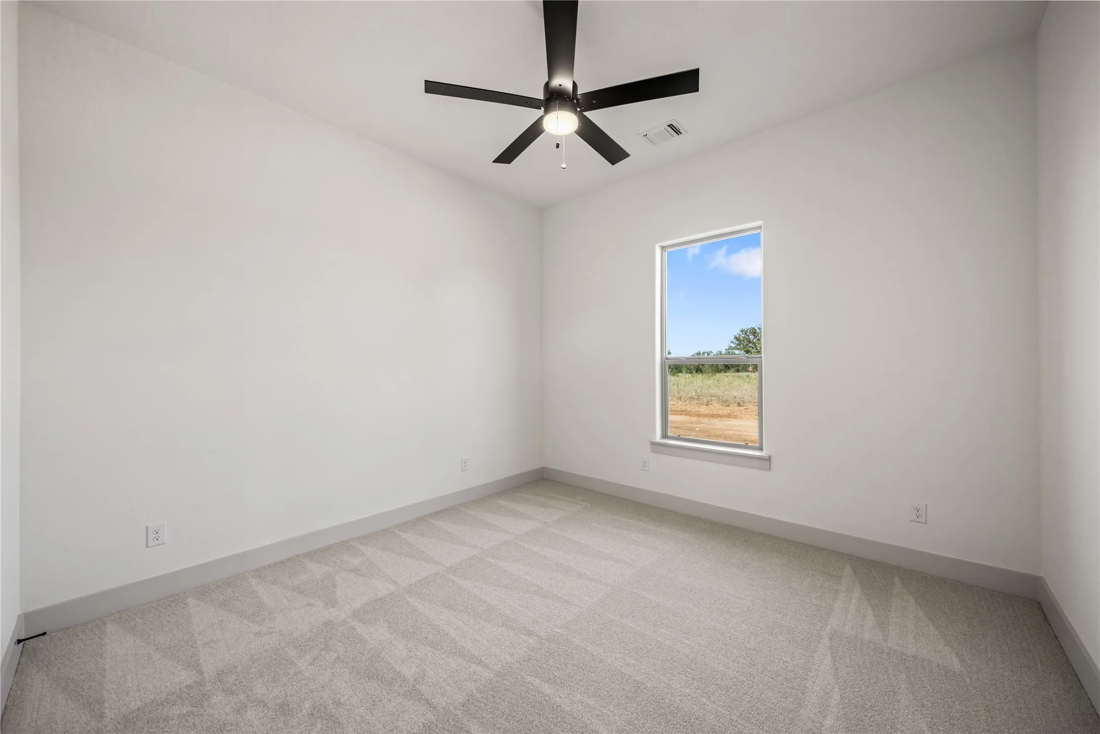 Spacious room featuring light gray carpeting with a geometric pattern, neutral wall paint, a single window, and a ceiling fan with integrated lighting