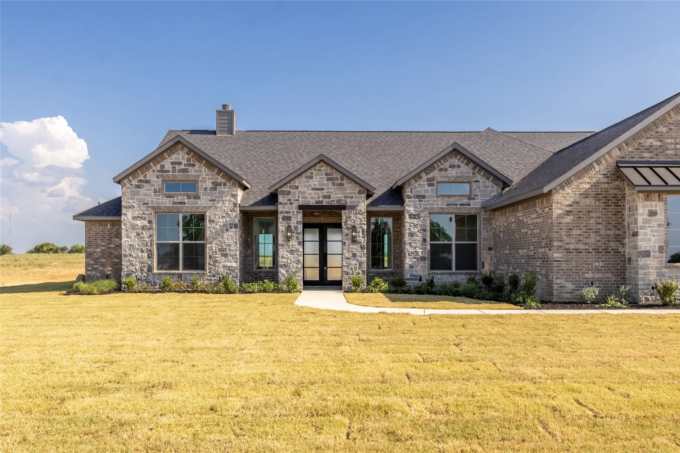 Stone and brick exterior featuring a dark asphalt shingle roof, gabled architectural elements, and a prominent double entry door with glass panels