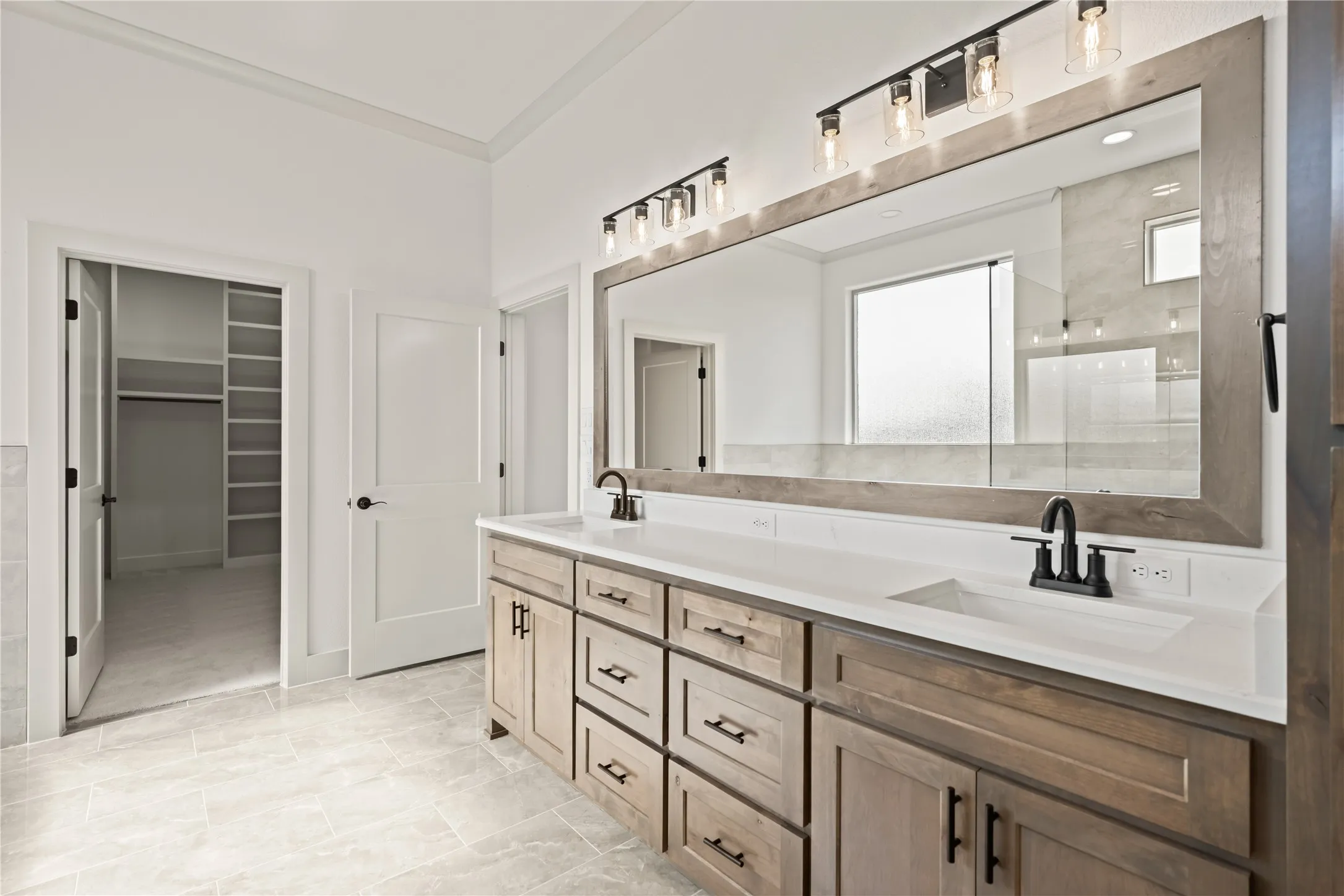 Spacious bathroom featuring a dual vanity with light wood-finish cabinetry, white countertops, and matte black fixtures