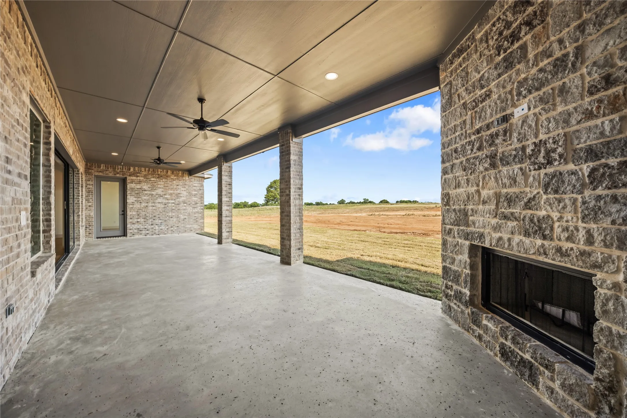 Spacious covered patio featuring a stone-clad fireplace and ceiling fans