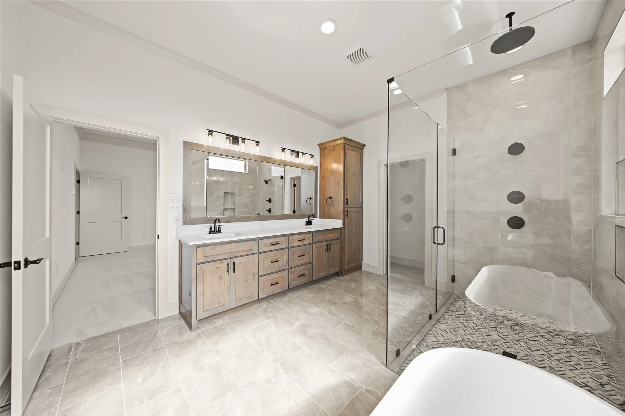 Spacious bathroom featuring a dual vanity with light wood-finish cabinetry, a large glass-enclosed shower with multiple showerheads, a freestanding soaking tub, and tile flooring