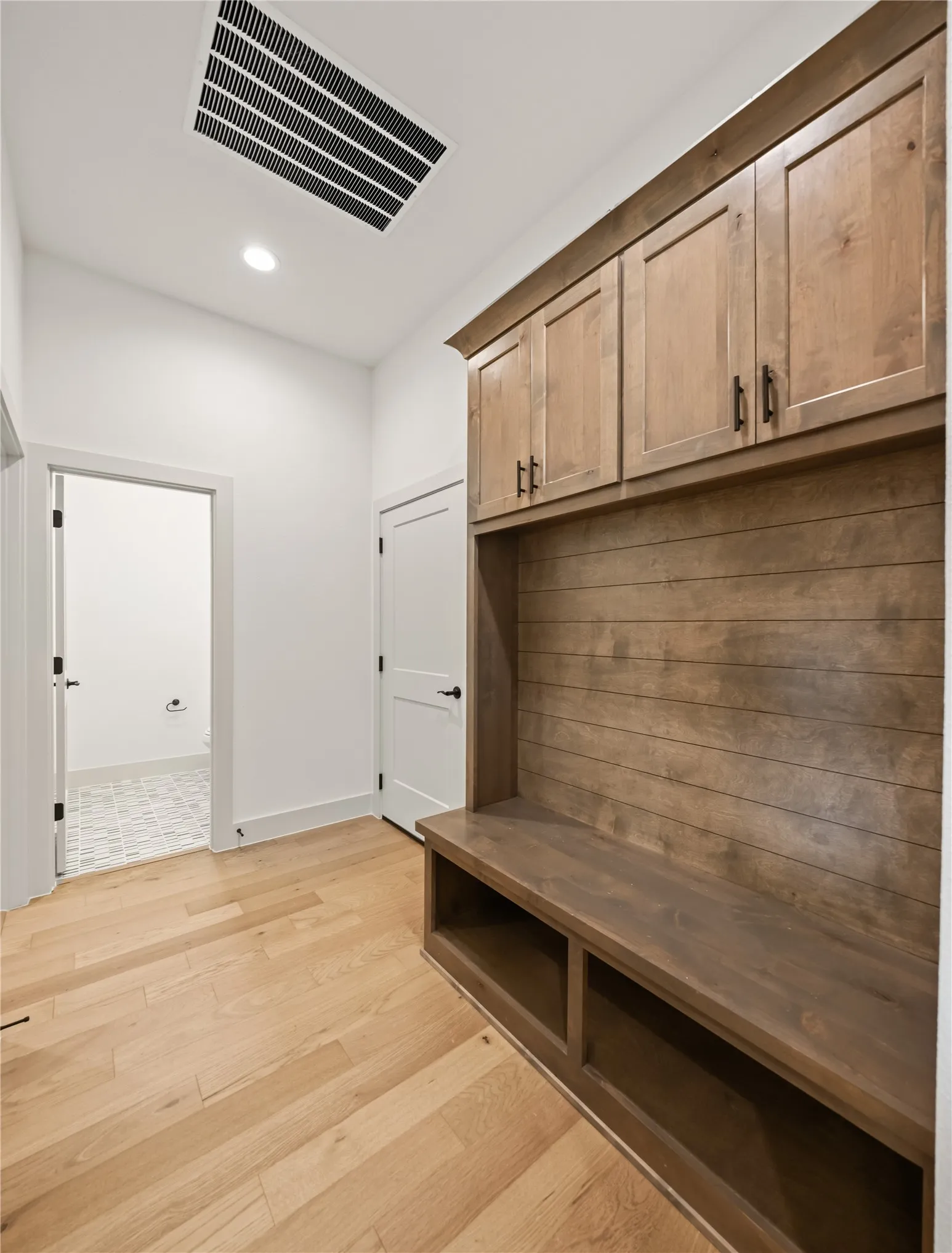 Mudroom featuring built-in wood cabinetry with matte black hardware, integrated bench seating with open storage, and horizontal wood paneling