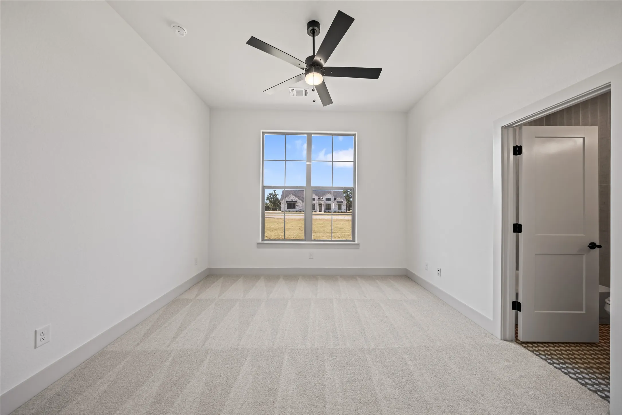 Bright room featuring a large window, neutral carpeting, a ceiling fan with light fixture, white walls, and white trim