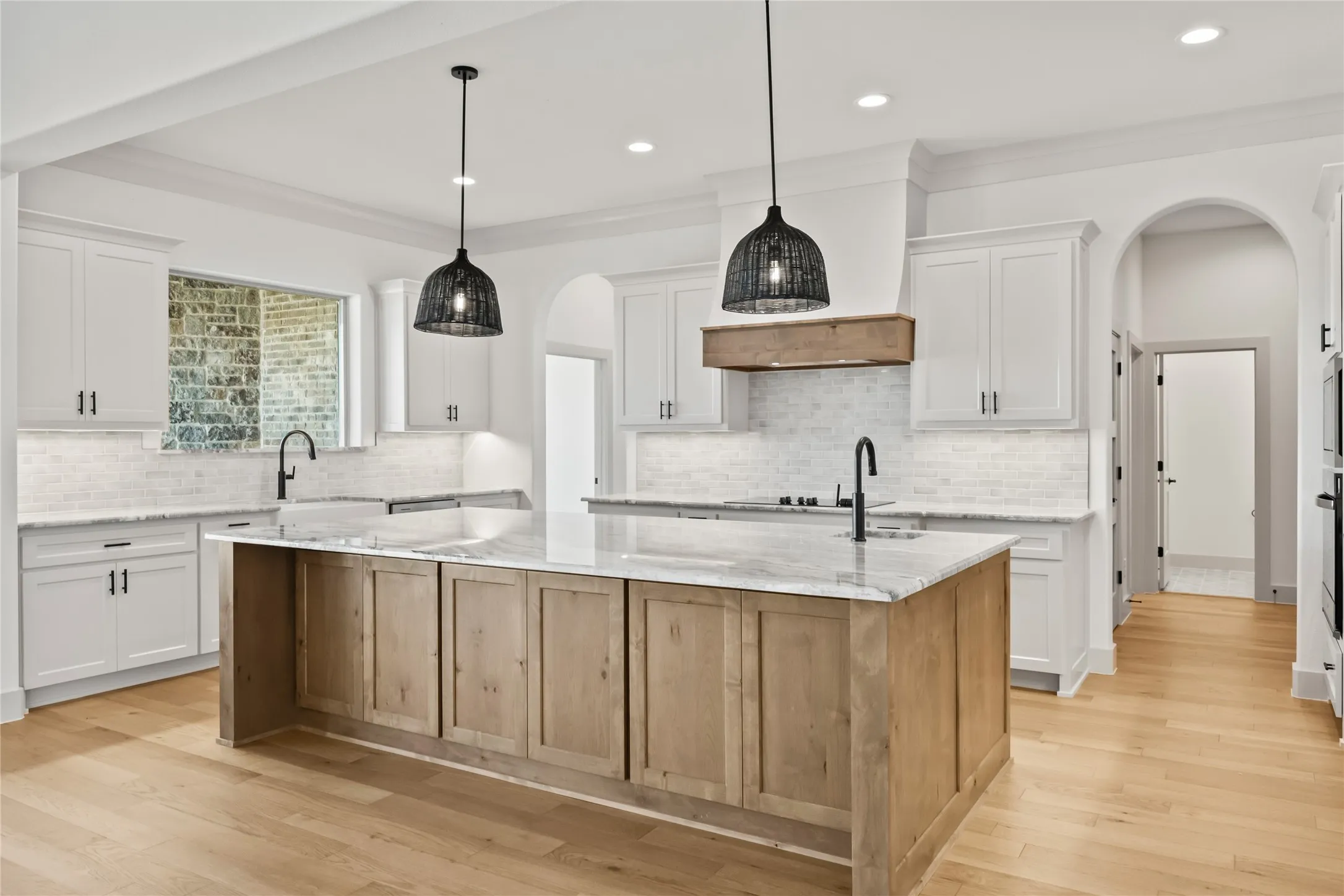 Spacious kitchen featuring a large central island with a light wood-finish base, dual pendant lighting, light-toned wood-finish flooring, white cabinetry, and a white subway tile backsplash