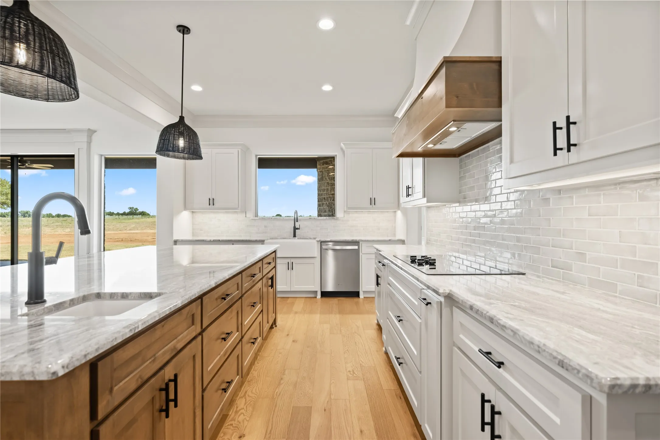 Gourmet kitchen featuring a wood-finish island with integrated sink, light wood-finish flooring, white cabinetry with matte black hardware, stone countertops, and a subway tile backsplash