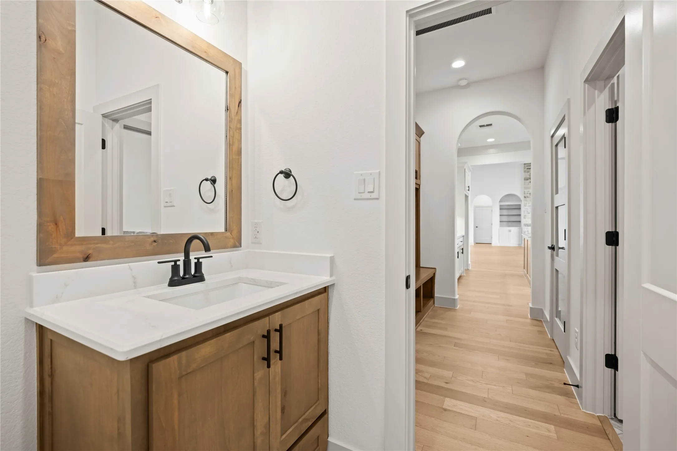 Bathroom vanity featuring a wood-finish cabinet, white countertop, integrated sink, and matte black faucet