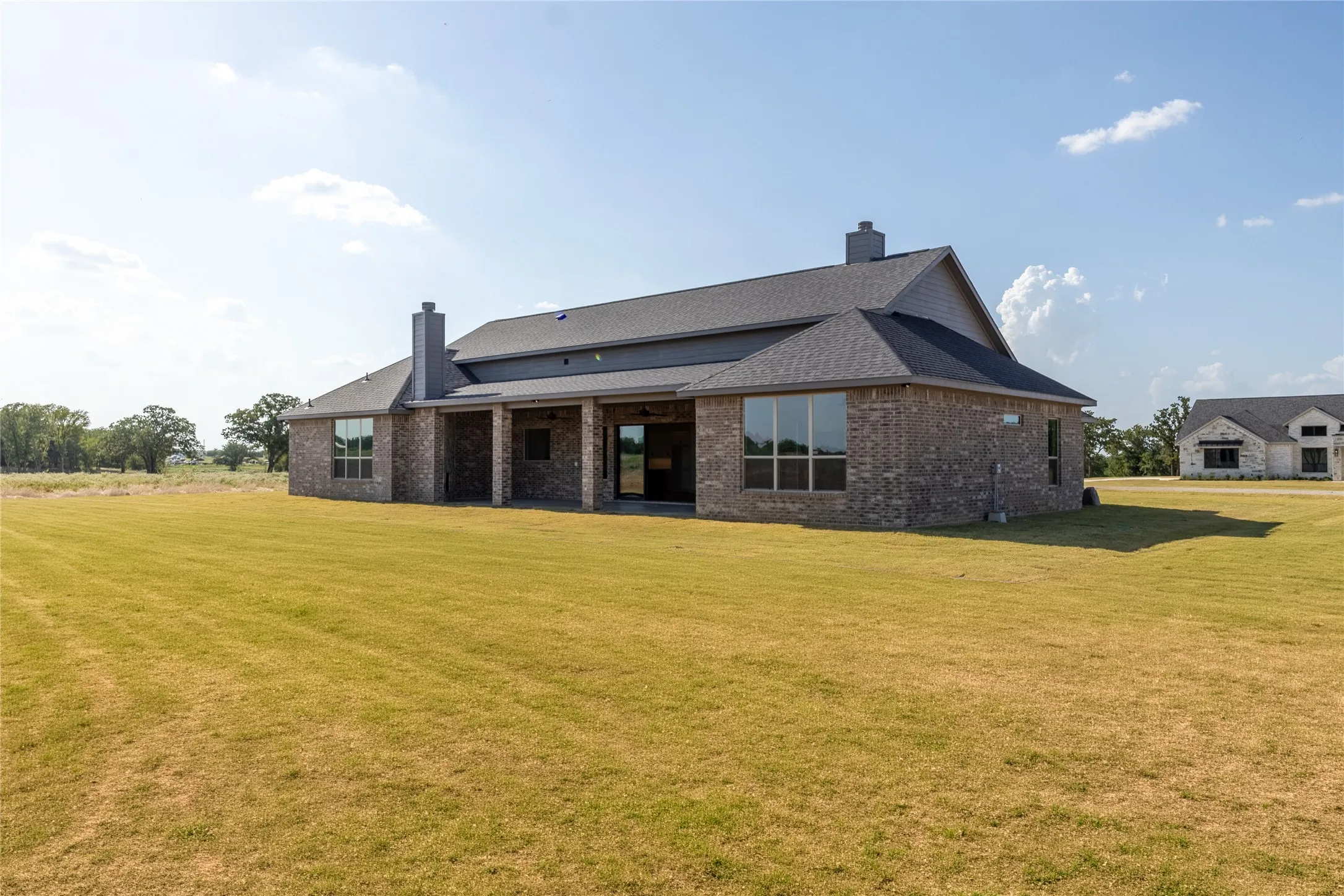Expansive lawn area encompassing a brick exterior with dark trim and multiple windows