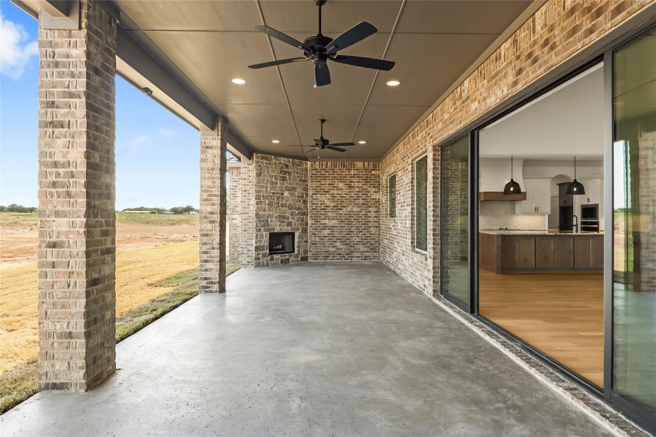 Covered patio featuring a brick fireplace, dual ceiling fans, recessed lighting, and large sliding glass doors opening to an interior space with wood-finish flooring