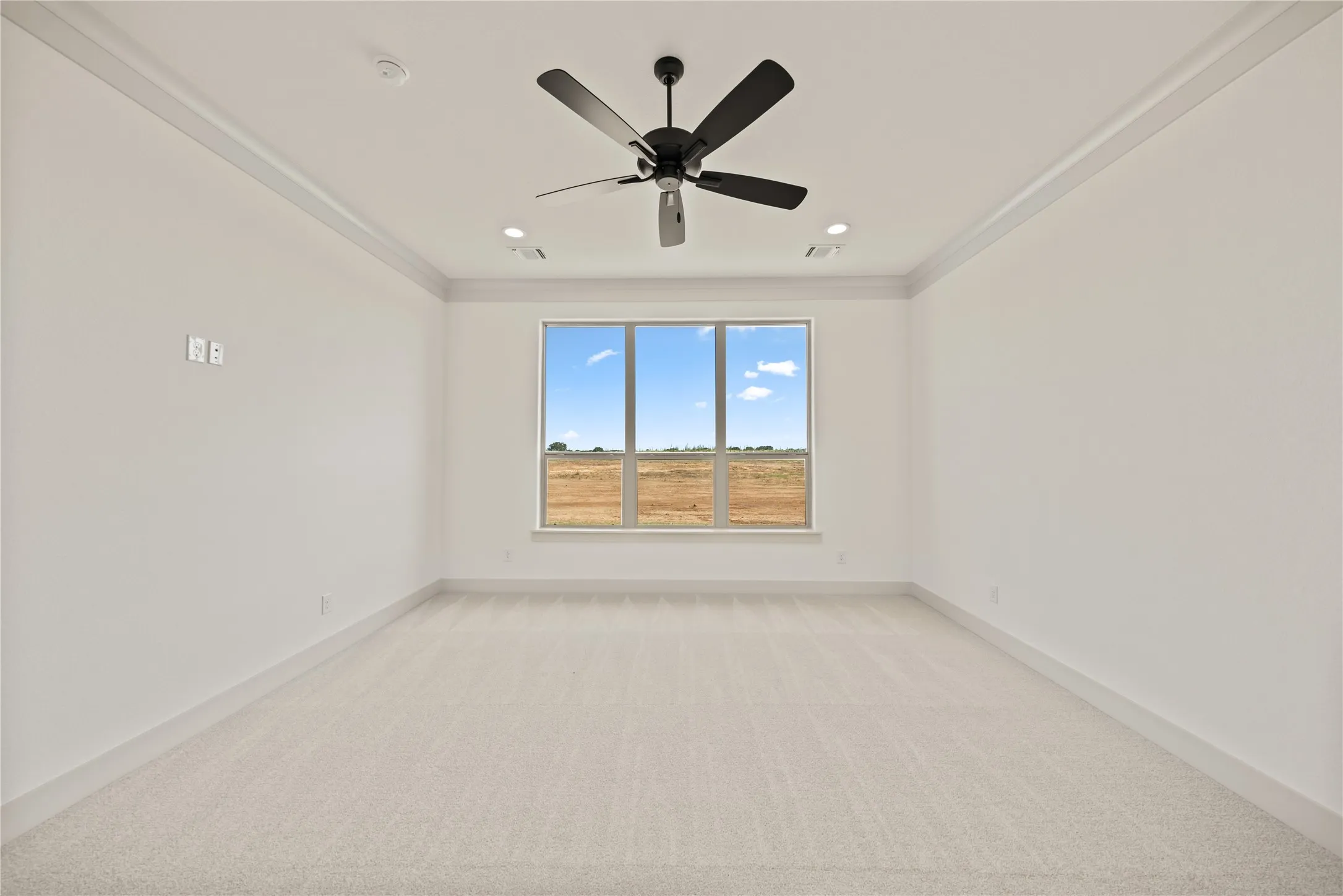 Spacious room featuring light-toned carpeting, a large window, a ceiling fan, recessed lighting, and crown molding