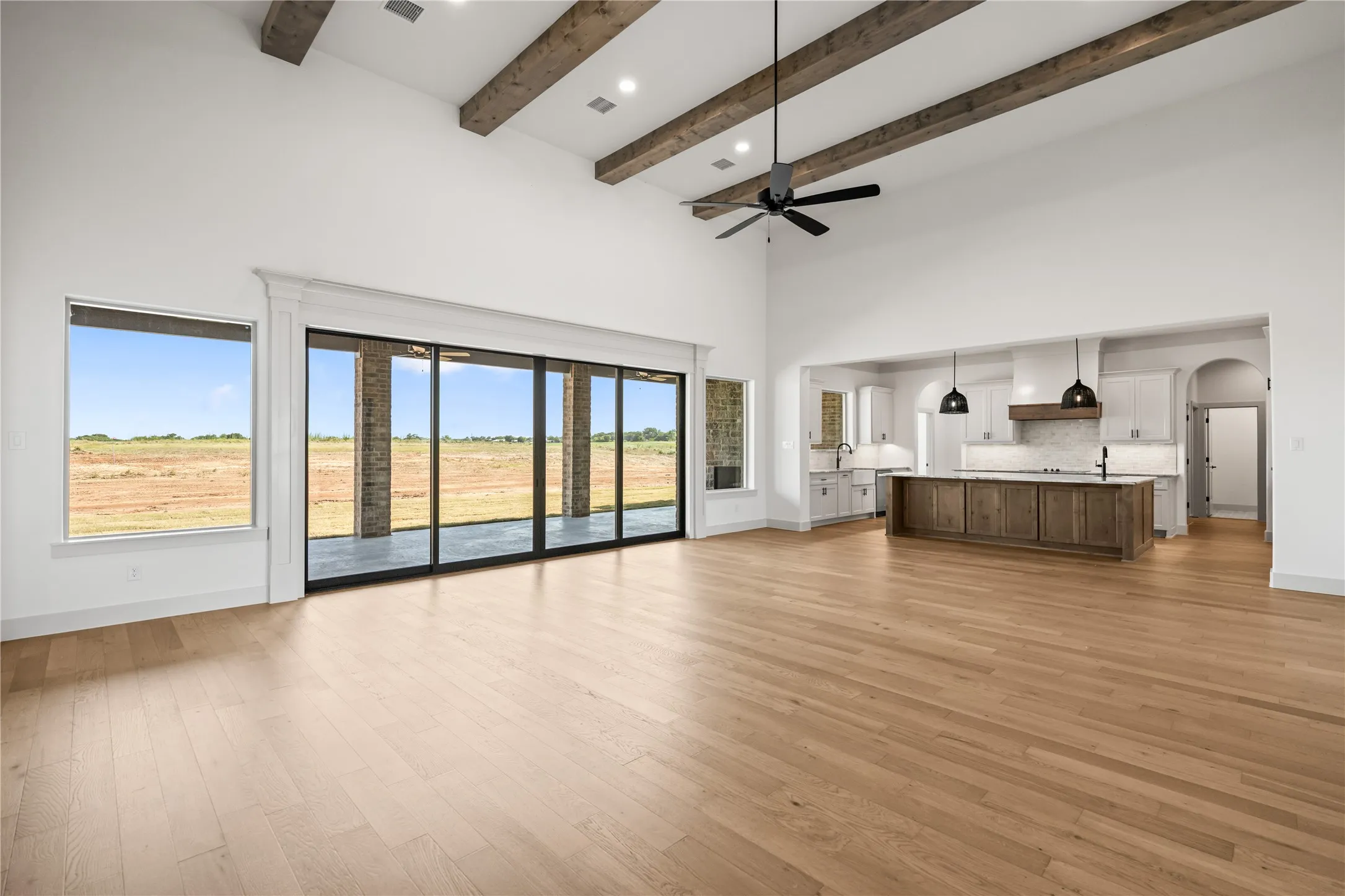 Open-concept living space featuring wood-finish flooring, a vaulted ceiling with exposed wood beams, and a ceiling fan