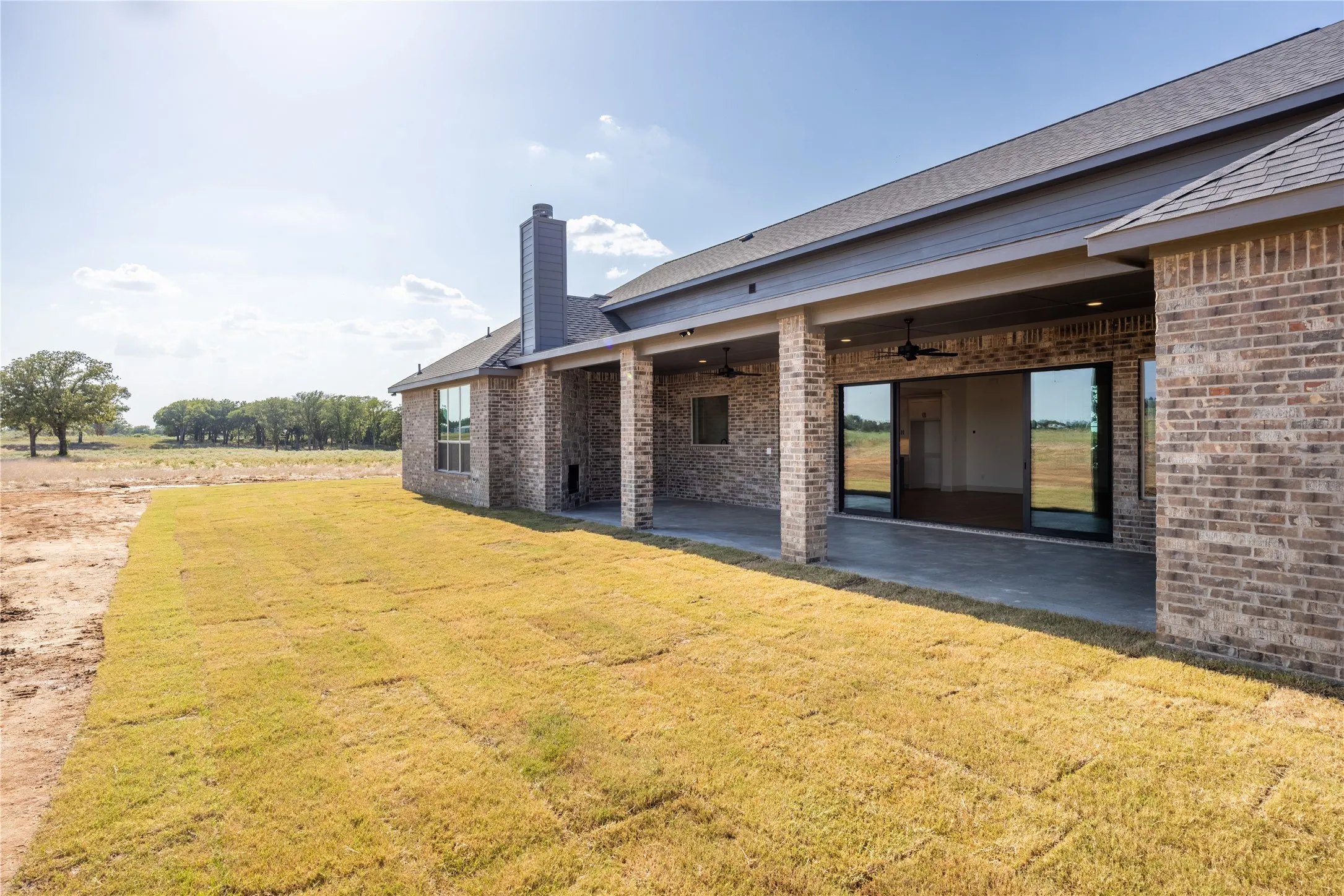 Expansive outdoor living area featuring a covered patio, brick exterior, and newly laid sod