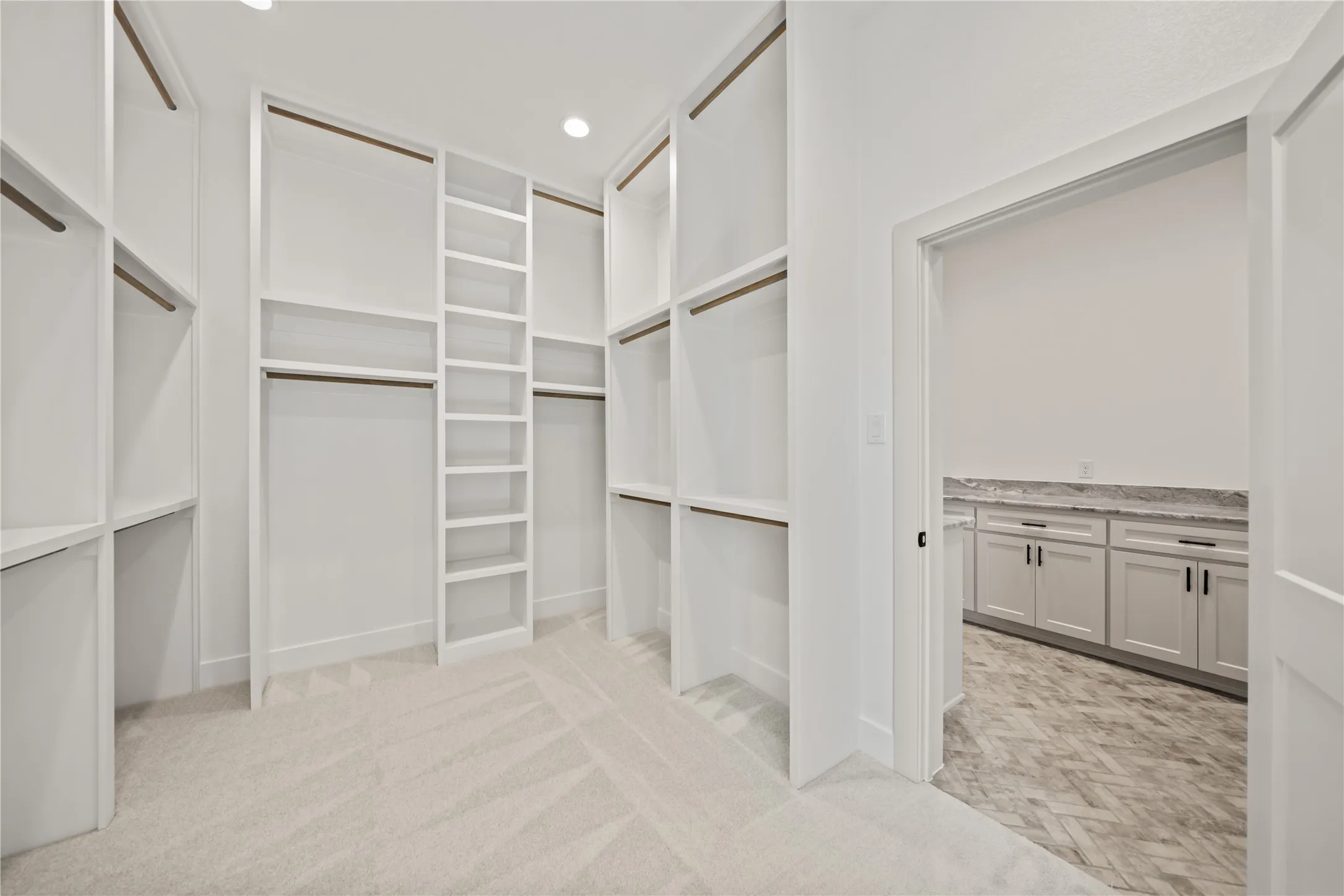 Expansive walk-in closet featuring custom white shelving, multiple hanging rods, and recessed lighting