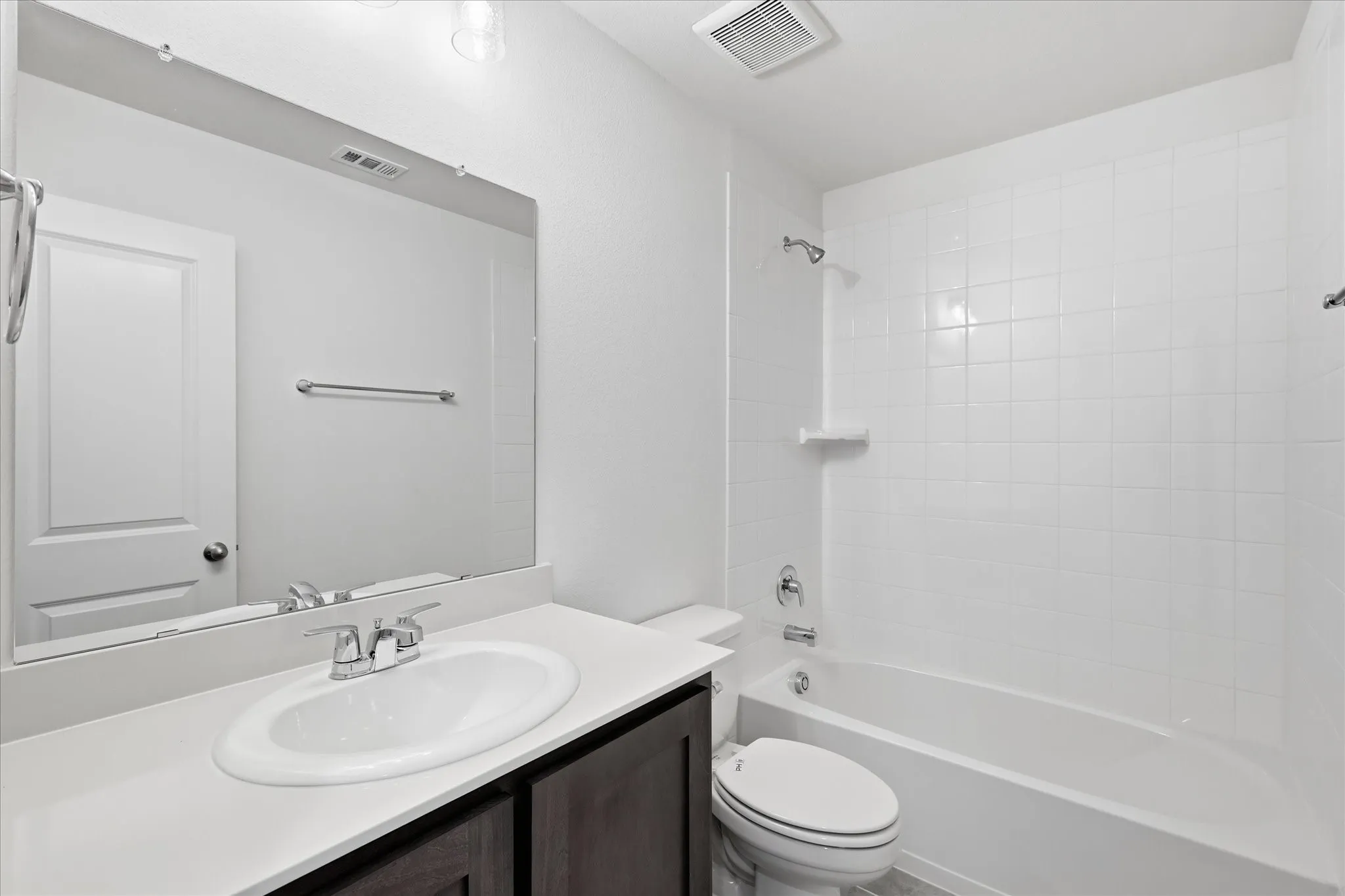 Full bathroom featuring a white tile tub/shower combination, dark wood-finish vanity with an oval undermount sink, and a large wall-mounted mirror