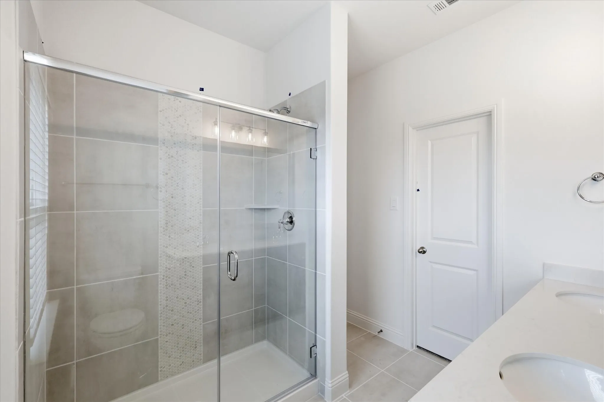 Glass-enclosed shower with subway tile surround, accent mosaic tile, built-in shelving, and polished chrome fixtures