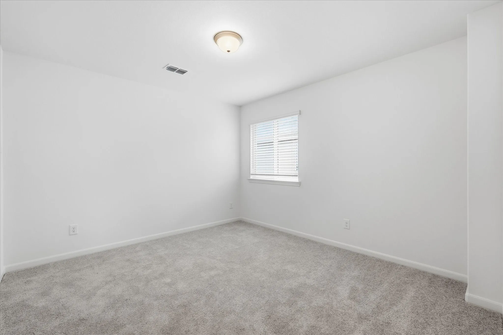 Carpeted room with a ceiling-mounted light fixture, a window featuring horizontal blinds, and clean white walls