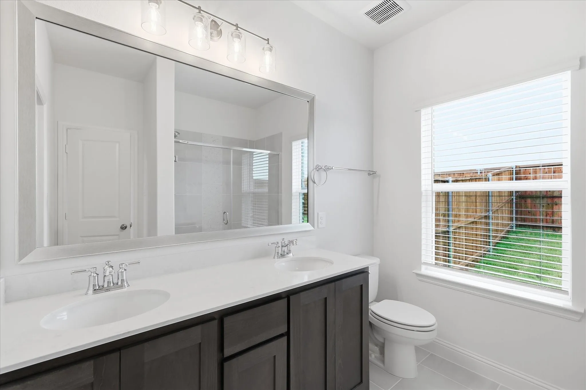 Bathroom featuring a dual vanity with dark wood-finish cabinetry, white countertop, and polished chrome fixtures