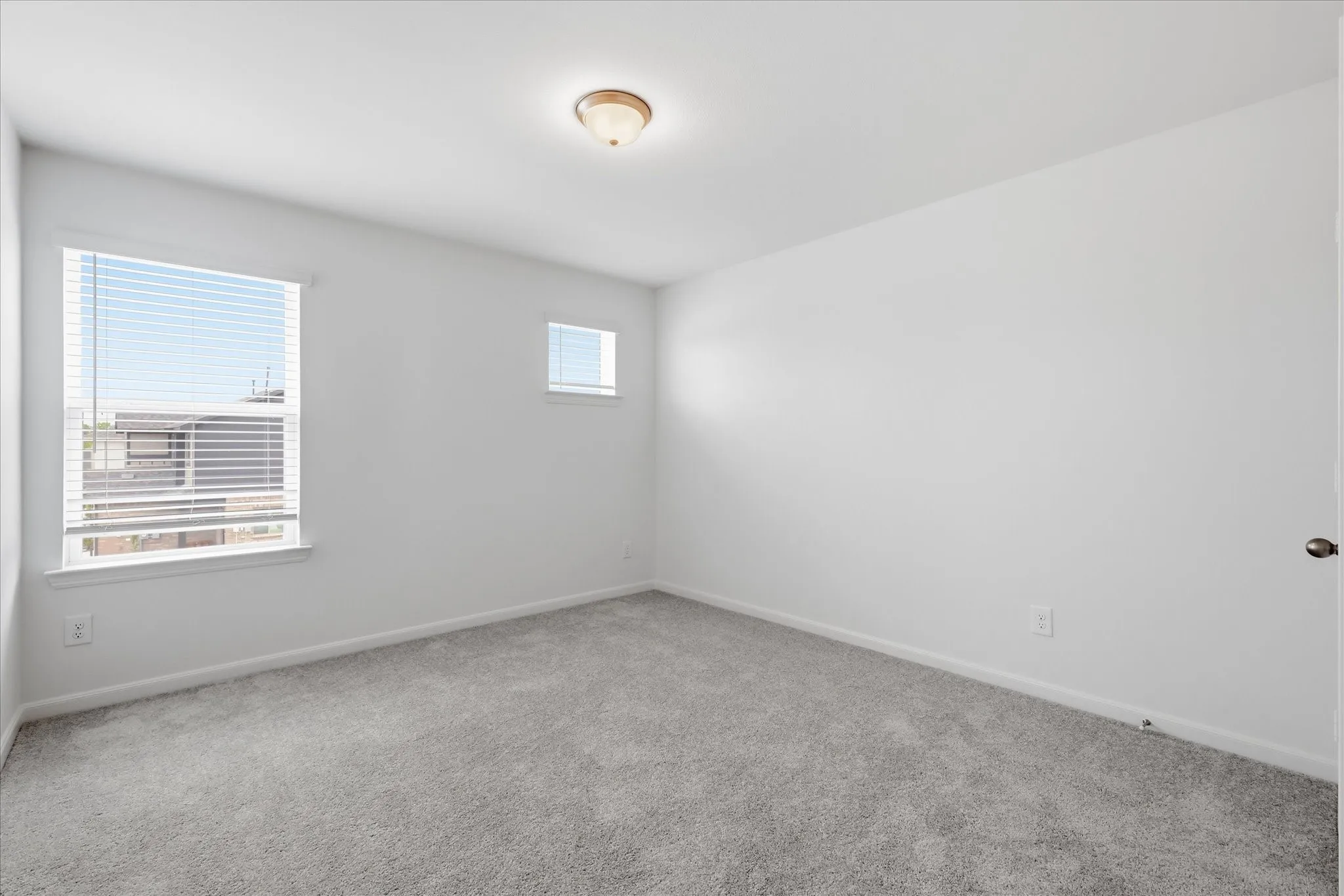 Bright interior space featuring light gray carpeting, neutral white walls, and two windows with horizontal blinds
