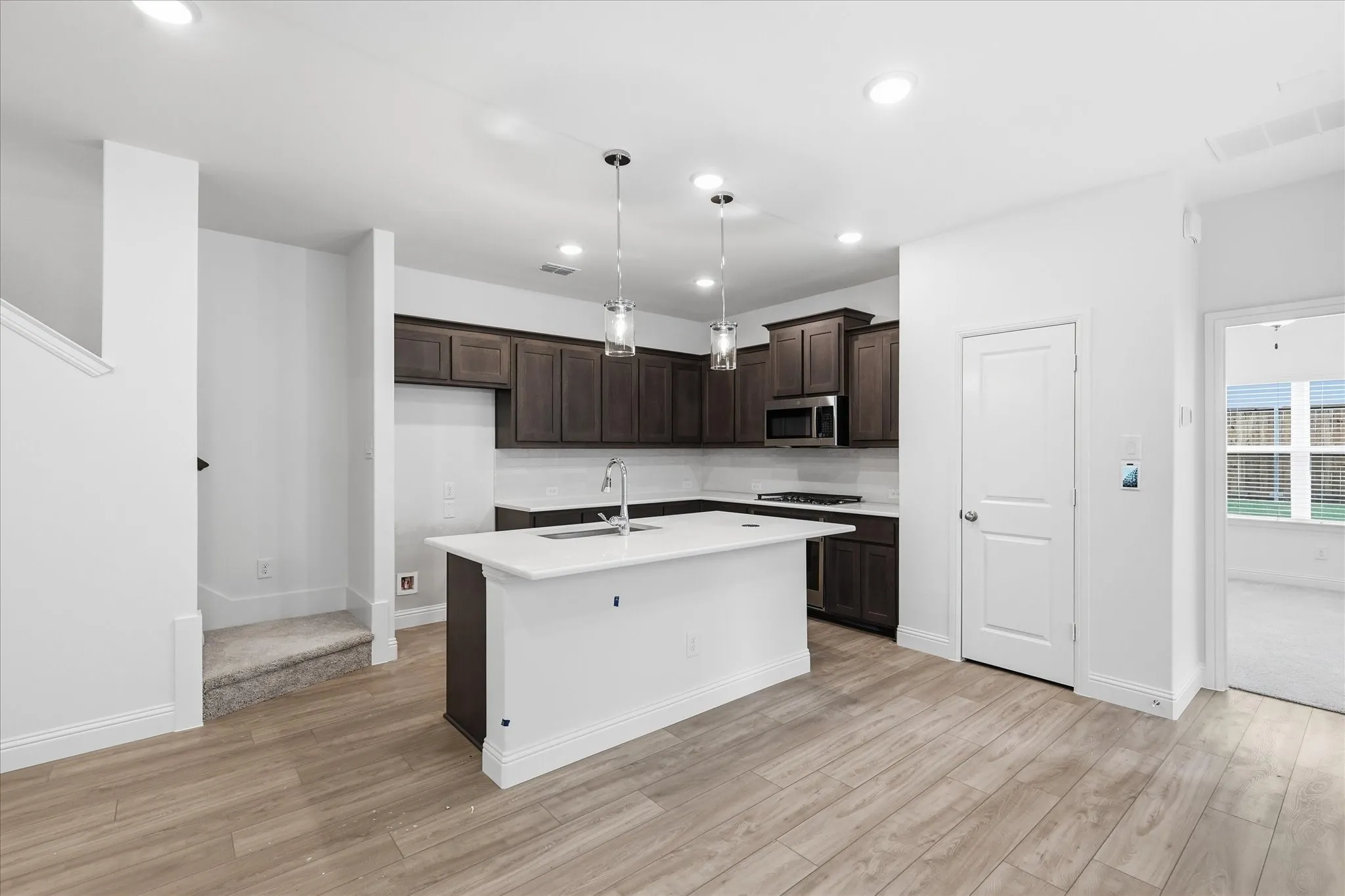 Kitchen featuring a central island with white countertop, dark wood-finish cabinetry, stainless steel appliances, and tile backsplash