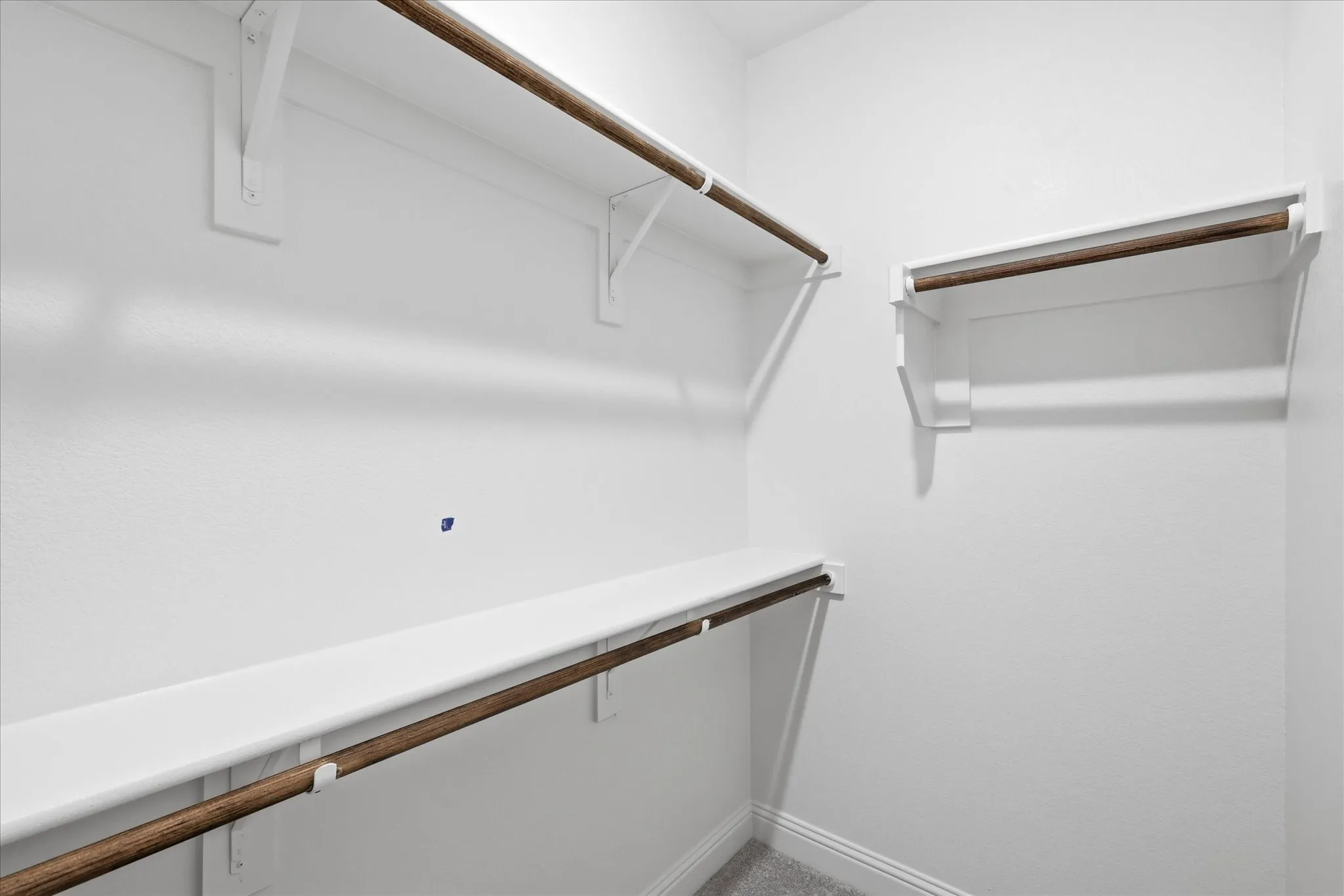 Walk-in closet featuring white walls, multiple shelving units, and wooden clothing rods