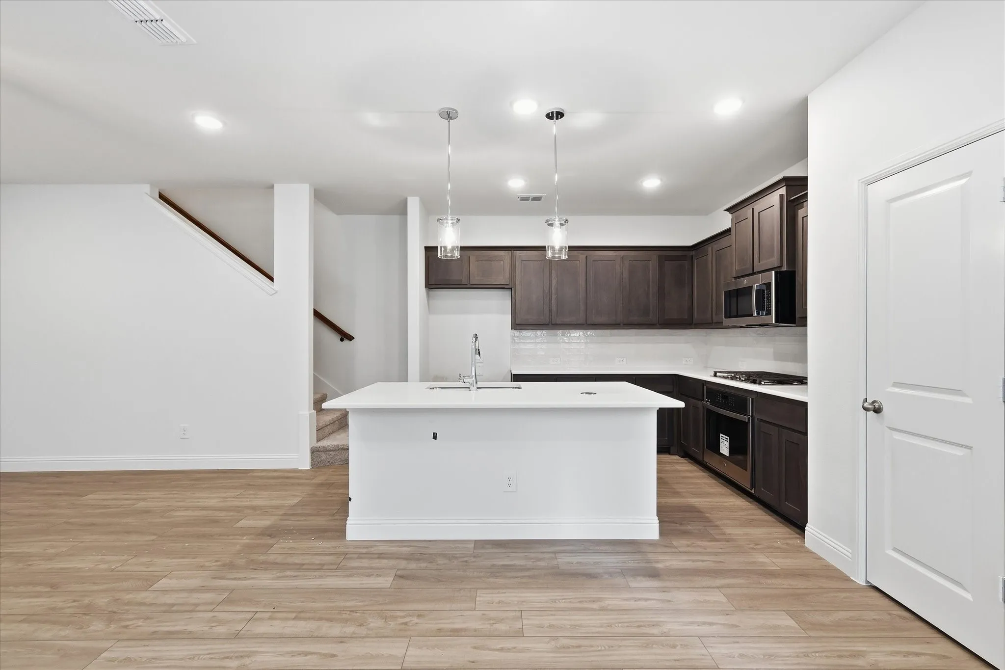 Bright kitchen featuring a central island, recessed lighting, wood-finish flooring, dark wood cabinetry, and stainless steel appliances