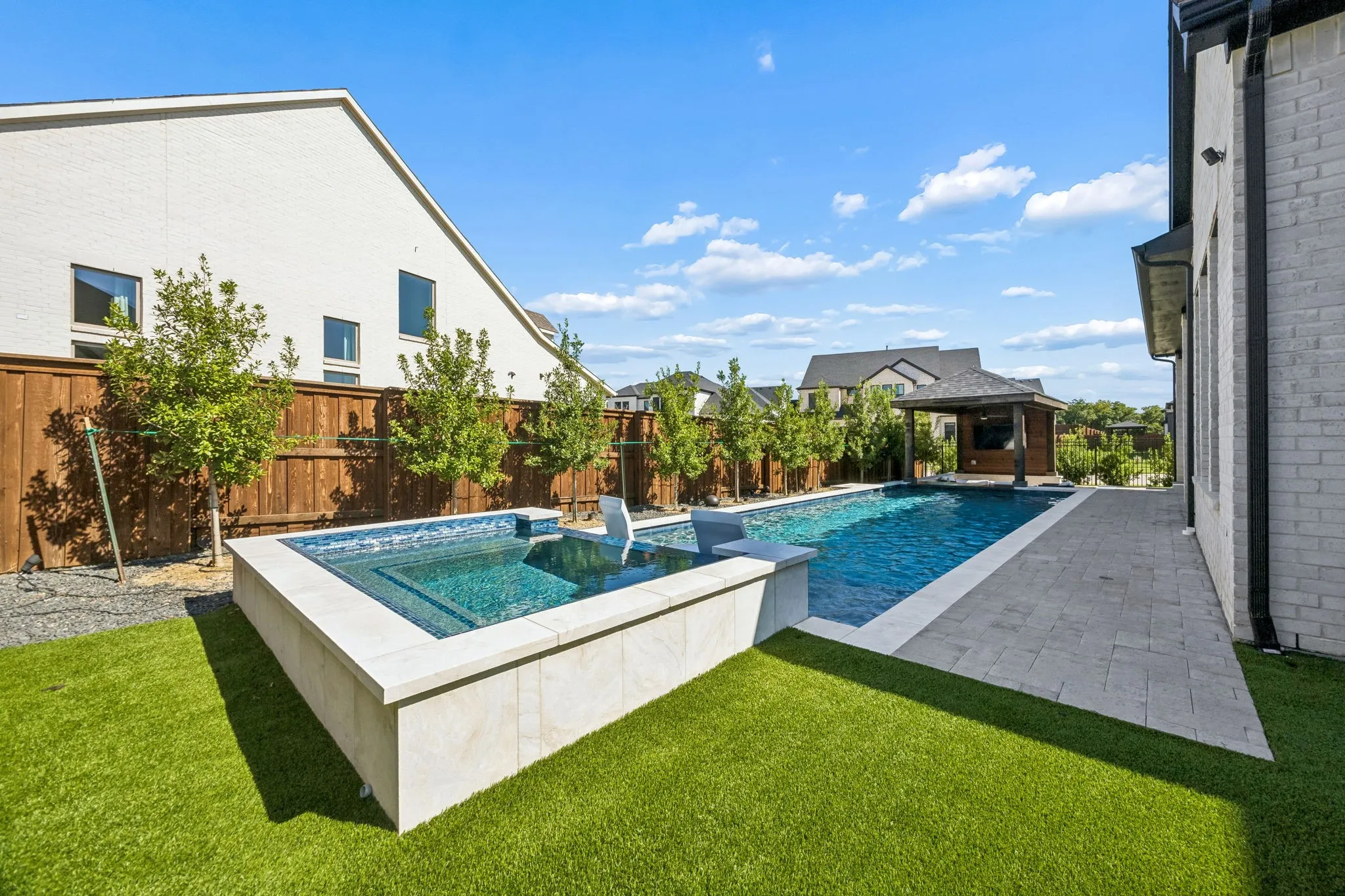 Rectangular swimming pool with integrated spa featuring blue tile and stone coping, surrounded by artificial turf and paver patio, sitting area and spa
