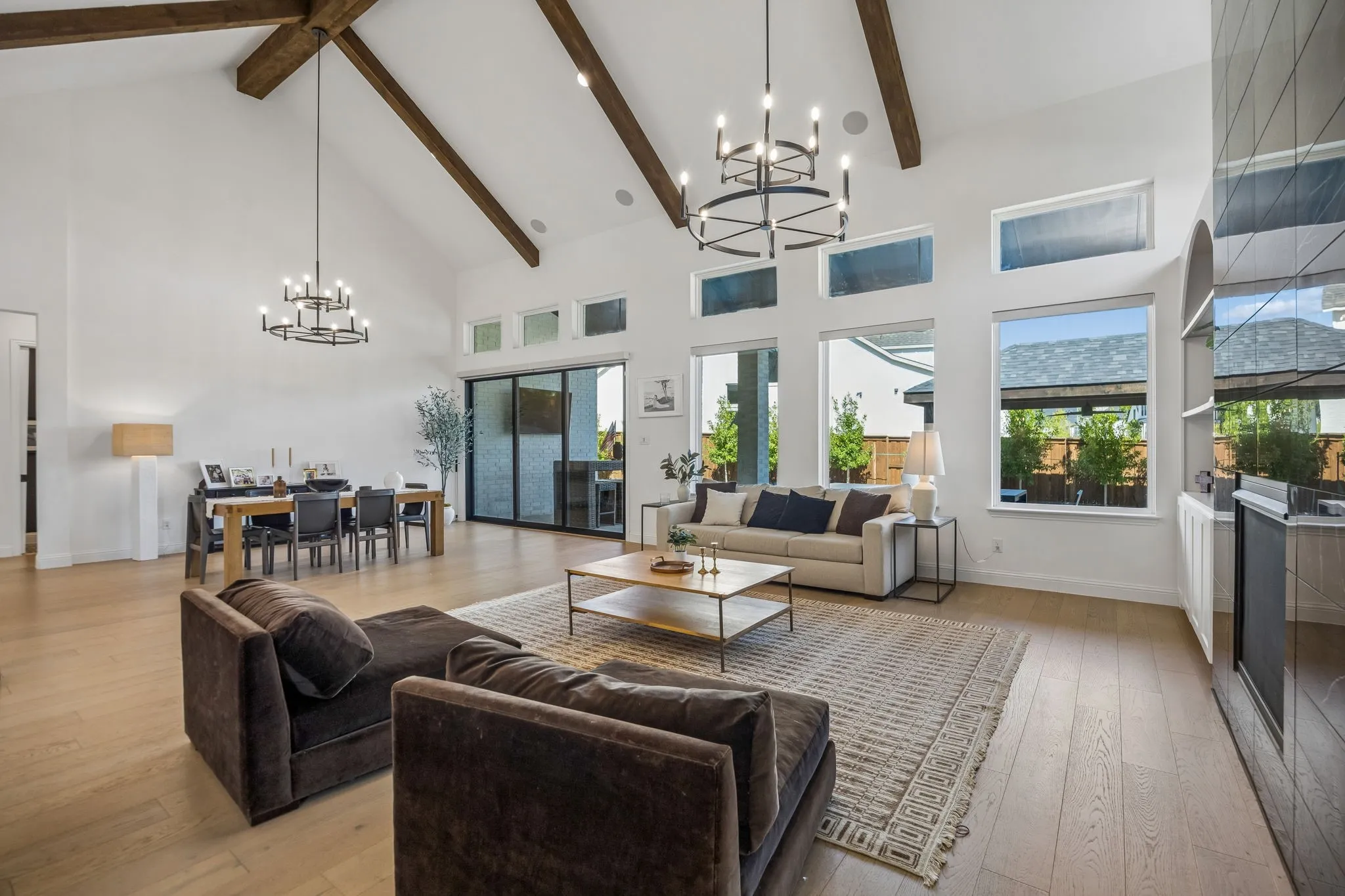 Spacious open-concept interior featuring vaulted ceilings with exposed wood beams, wood-finish flooring, and a floor-to-ceiling black stone fireplace