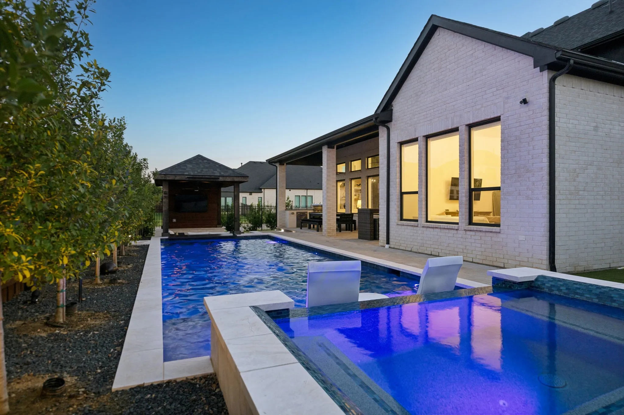 Backyard oasis featuring a rectangular pool with integrated spa, a separate poolside pavilion, and a covered patio