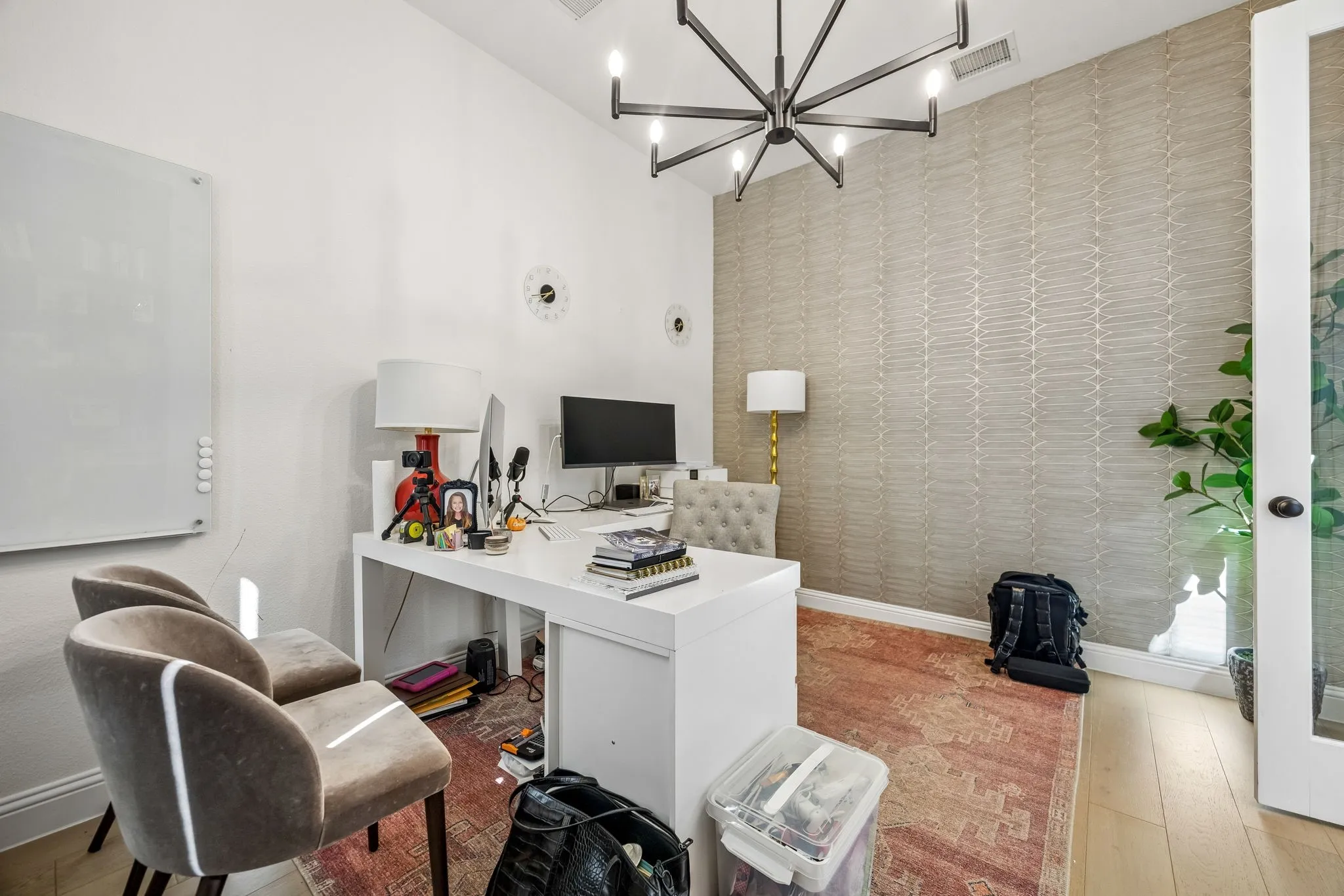 Dedicated office space featuring light wood-finish flooring, a contemporary chandelier, textured accent wall, a whiteboard, and a glass-paneled door