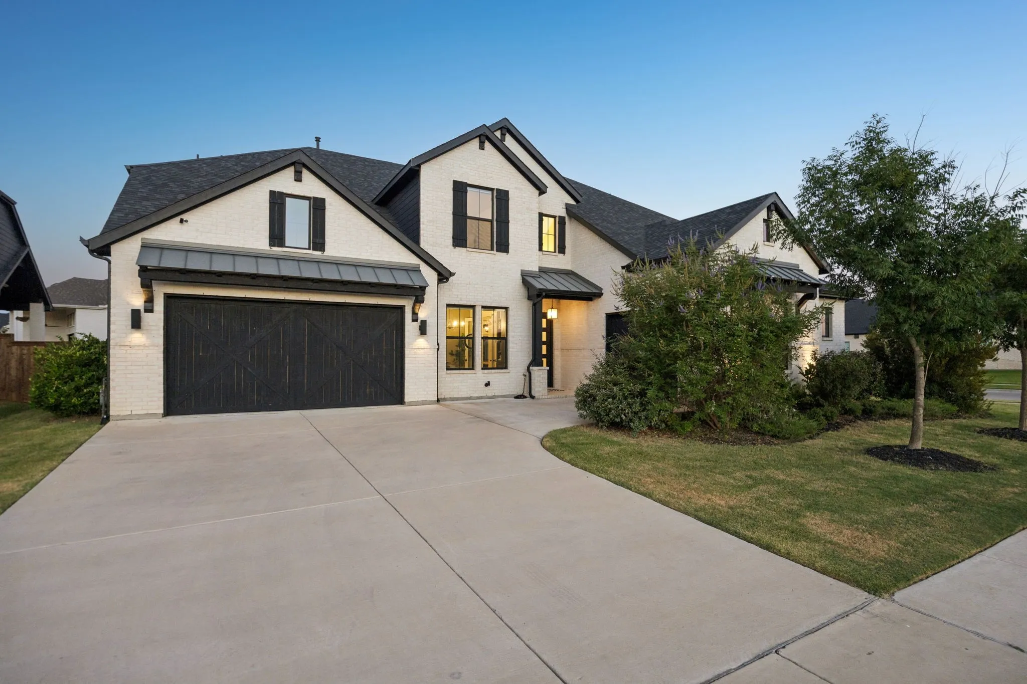 Modern farmhouse exterior featuring light brick, a dark shingle roof, and a dark wood-finish garage door