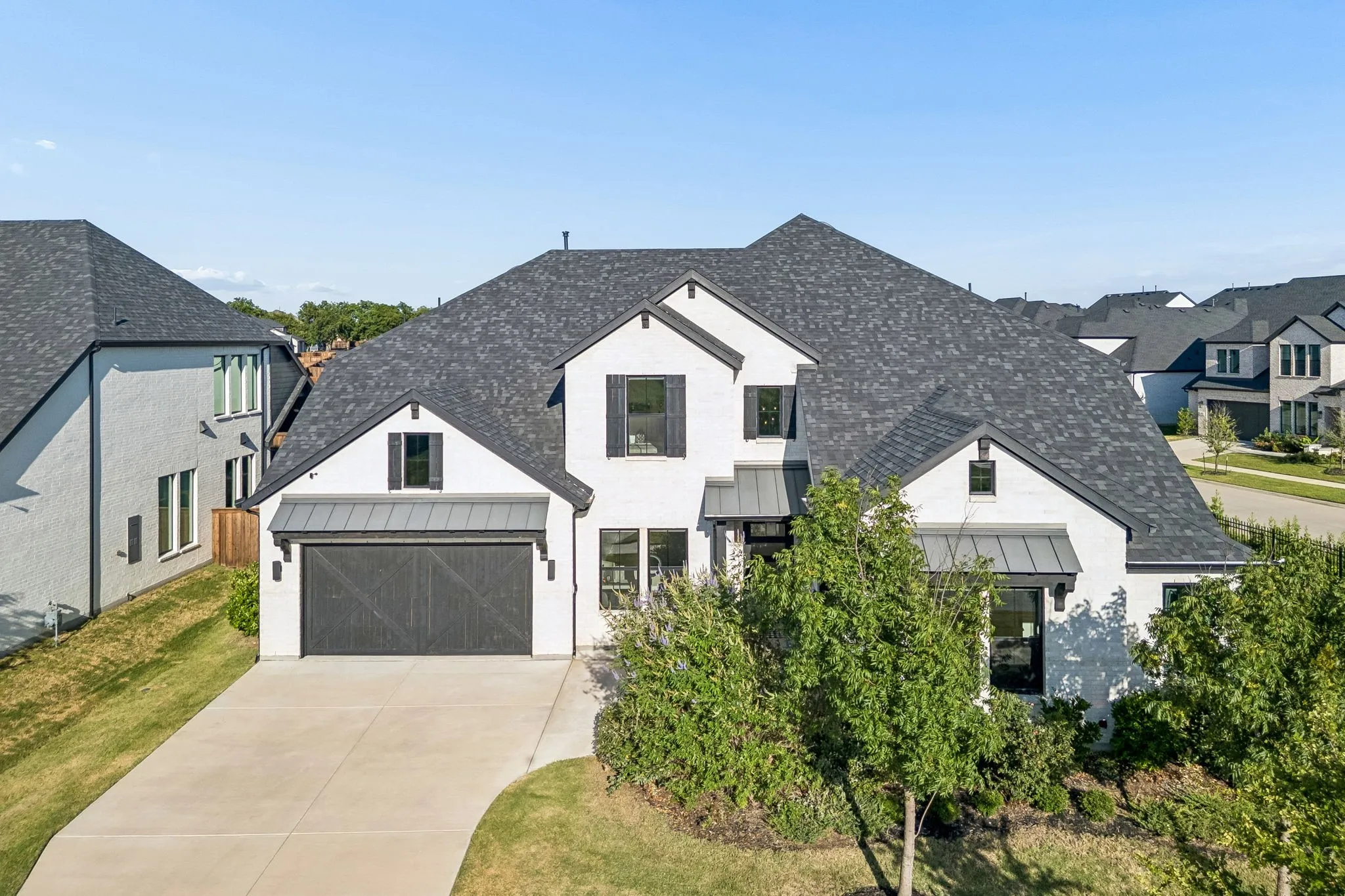 Modern farmhouse exterior featuring white painted brick, a dark shingle roof, black-framed windows, a dark garage door, and a concrete driveway