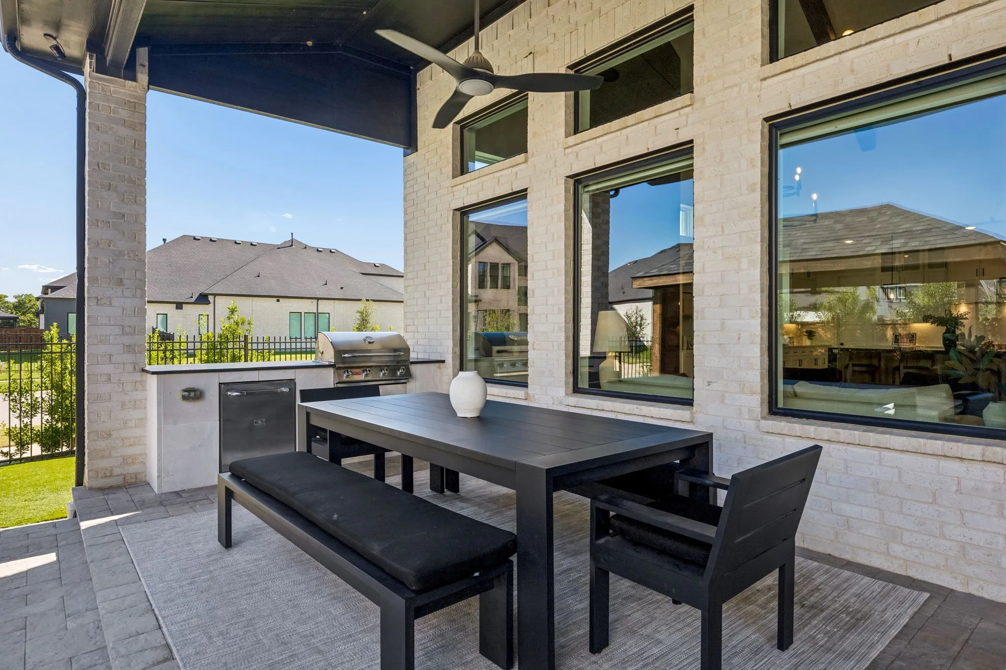 Covered patio featuring an outdoor kitchen with built-in grill and beverage cooler, ceiling fan, large format windows, and brick exterior