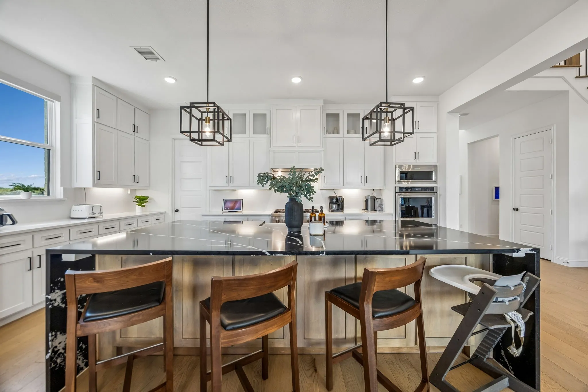 Spacious kitchen featuring an oversized island with a dark stone countertop, white shaker cabinetry, stainless steel built-in appliances, and wood-finish flooring