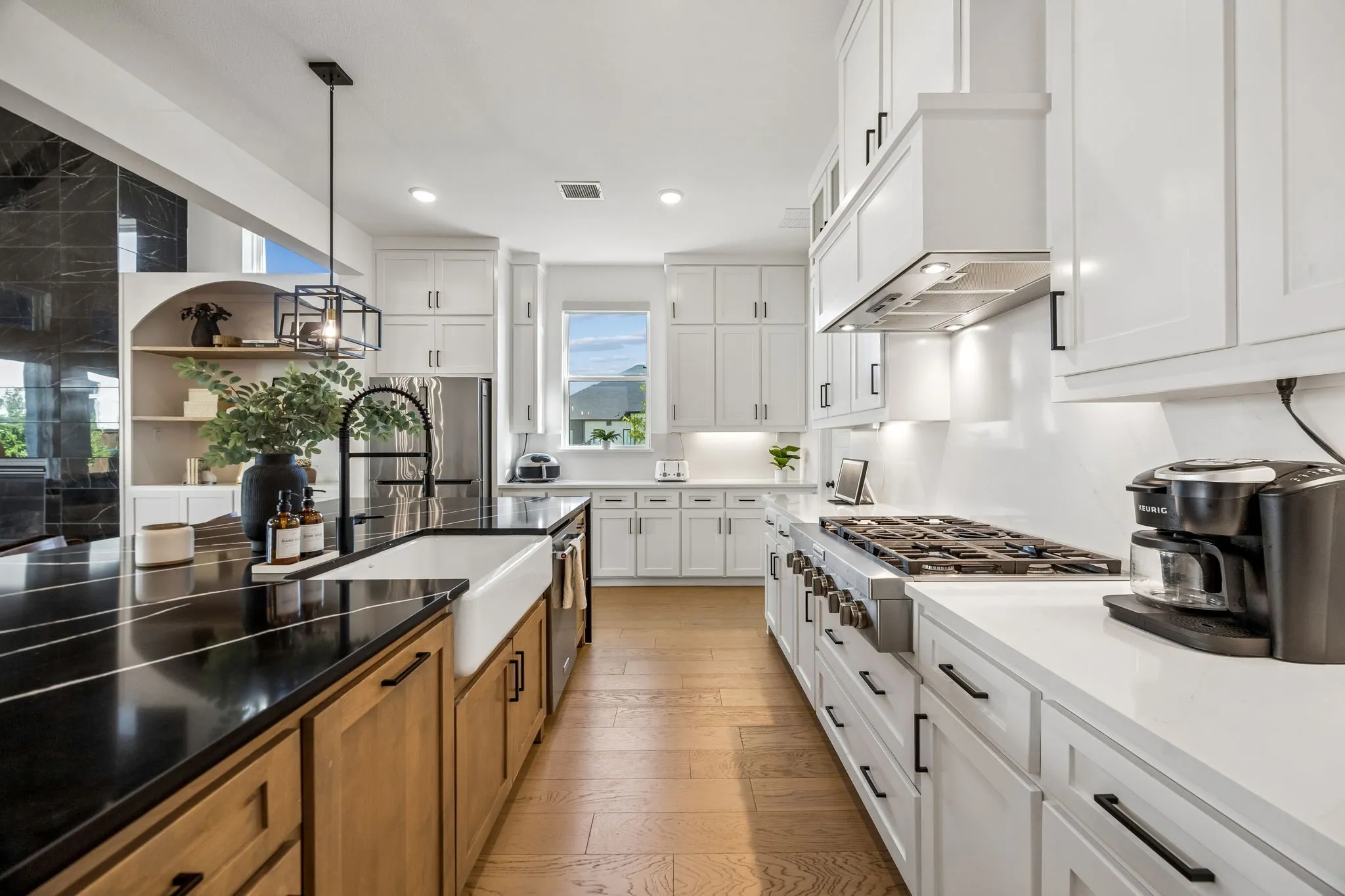 Gourmet kitchen featuring a large island with a farmhouse sink, white shaker cabinetry, stainless steel appliances, and wood-finish flooring