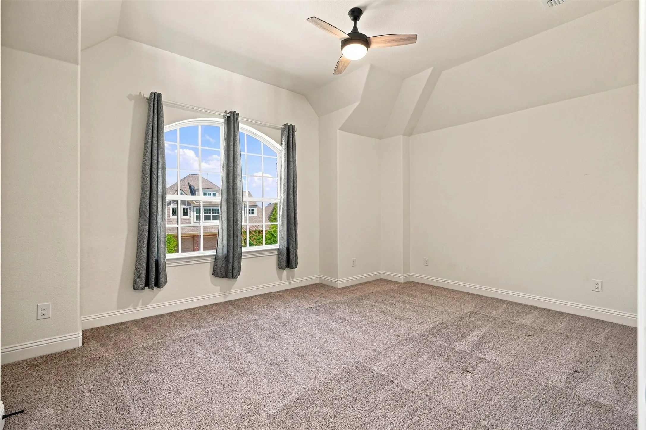 Carpeted room featuring an arched window, a ceiling fan with light fixture, and white trim