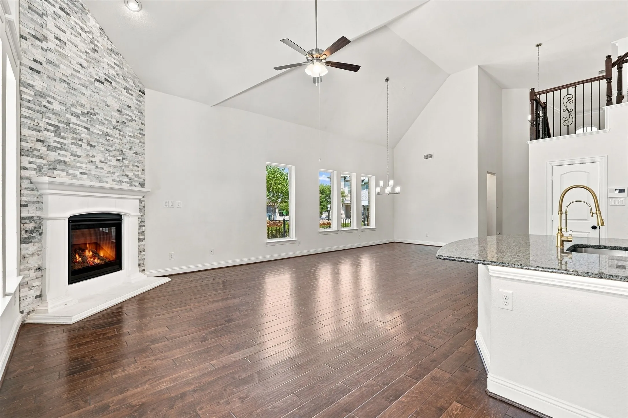 Vaulted living space featuring a stacked stone fireplace with a white mantel, dark wood-finish flooring, and multiple windows
