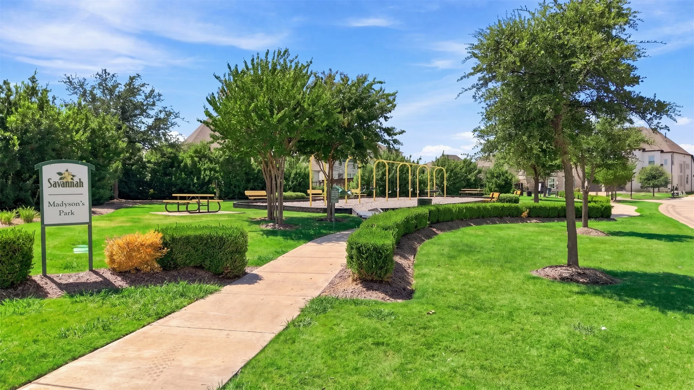 Community park area featuring a playground, picnic seating, a concrete pathway, and mature landscaping
