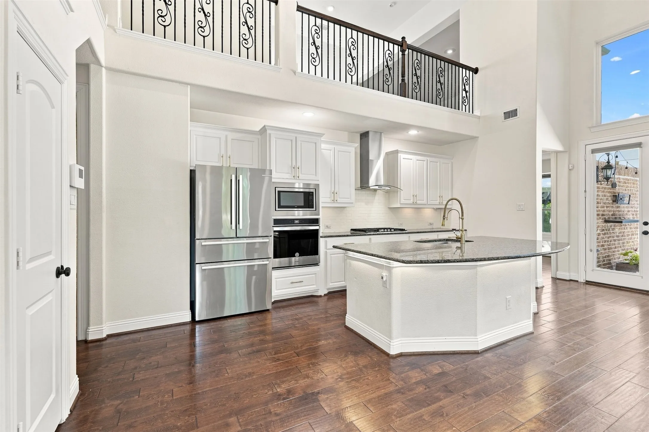 Open-concept kitchen featuring an oversized island with granite countertop, stainless steel appliances, white cabinetry, and wood-finish flooring