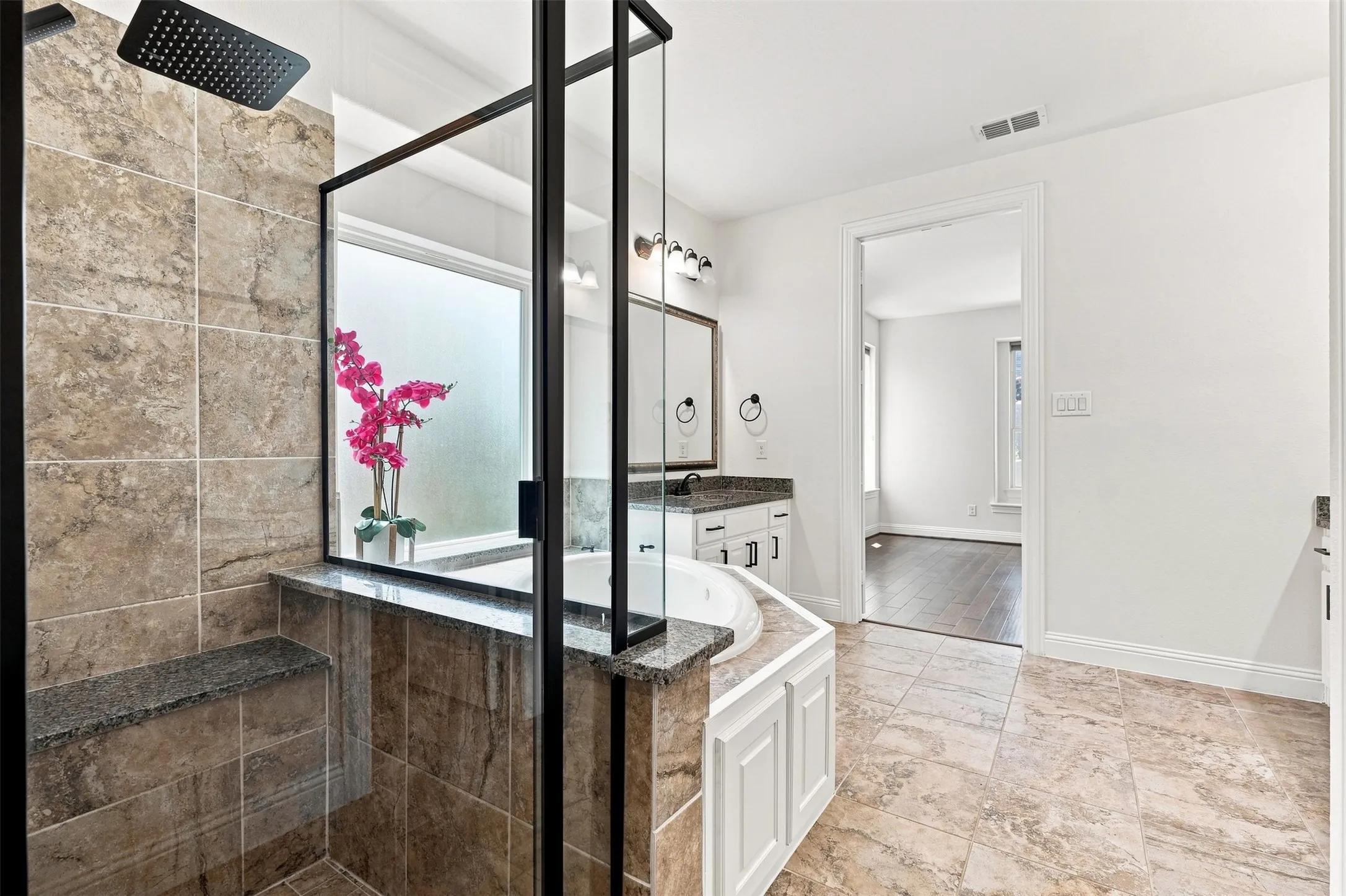 Spacious bathroom featuring a frameless glass shower enclosure with a built-in bench, a soaking tub with granite surround, a vanity with granite countertop, and tiled flooring