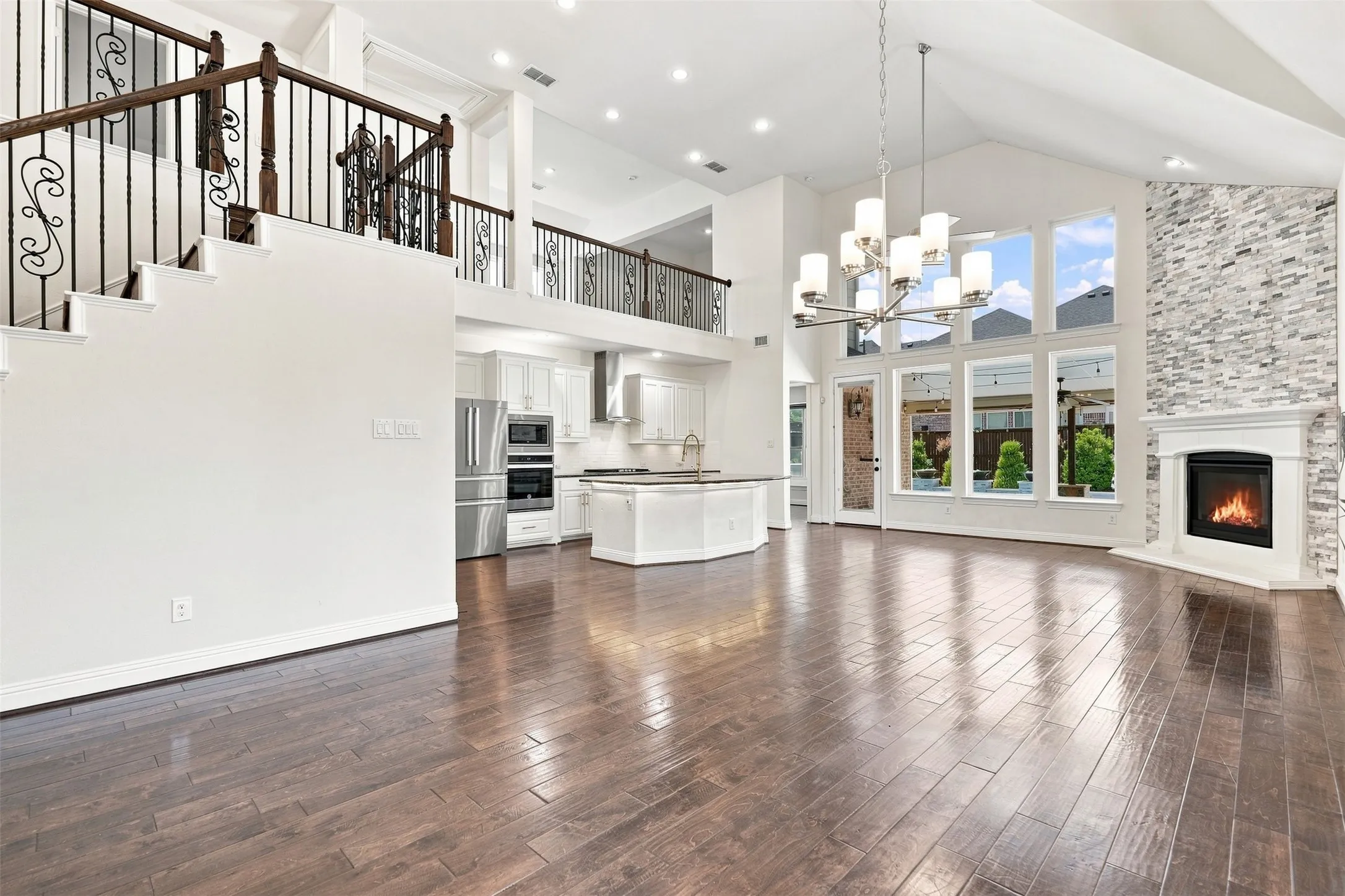 Expansive open concept living area featuring dark wood-finish flooring, a two-story vaulted ceiling, and a fireplace with a stacked stone surround