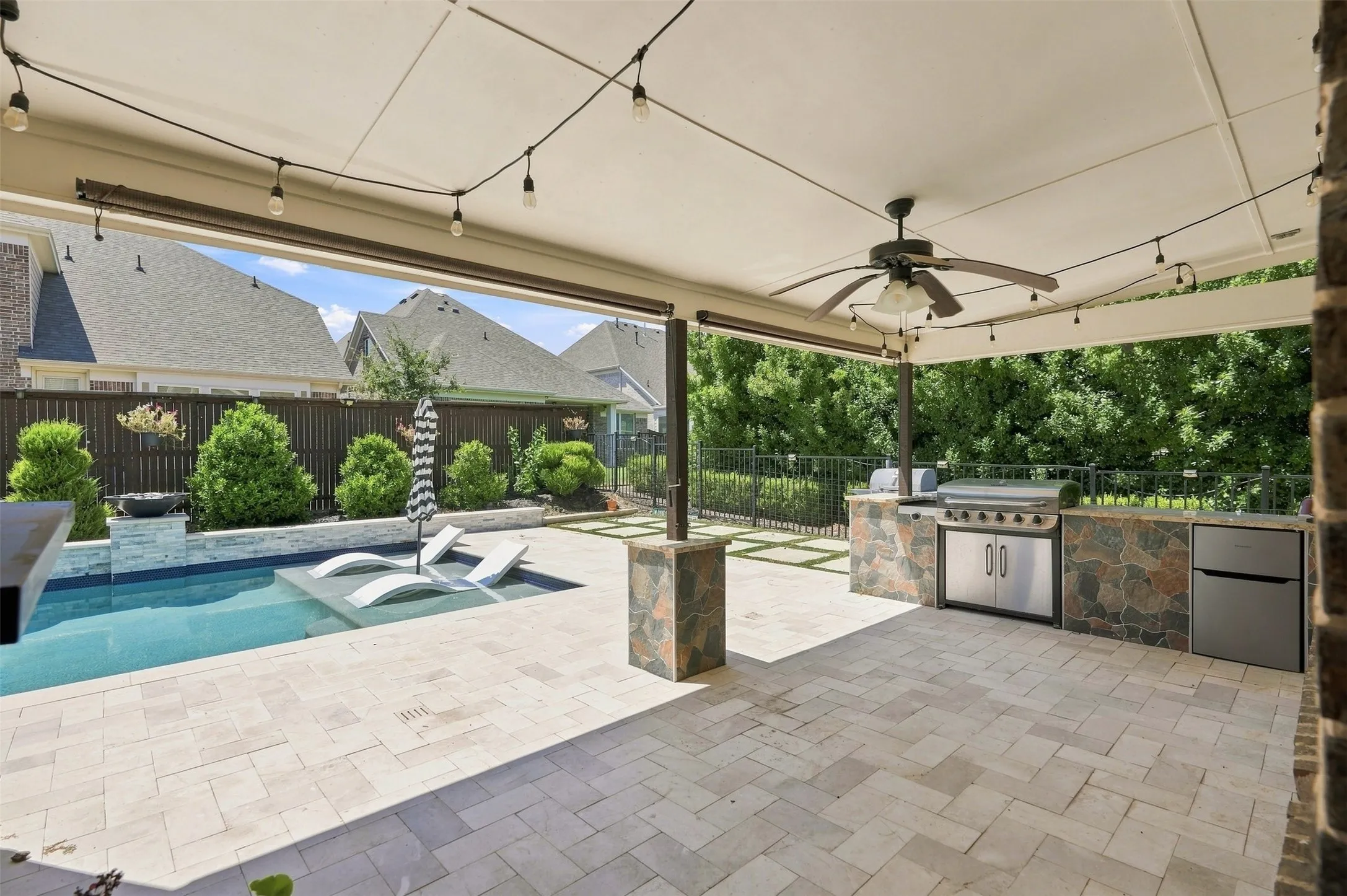 Covered patio featuring an outdoor kitchen with integrated grill and refrigerator, paver flooring, string lighting, and a ceiling fan