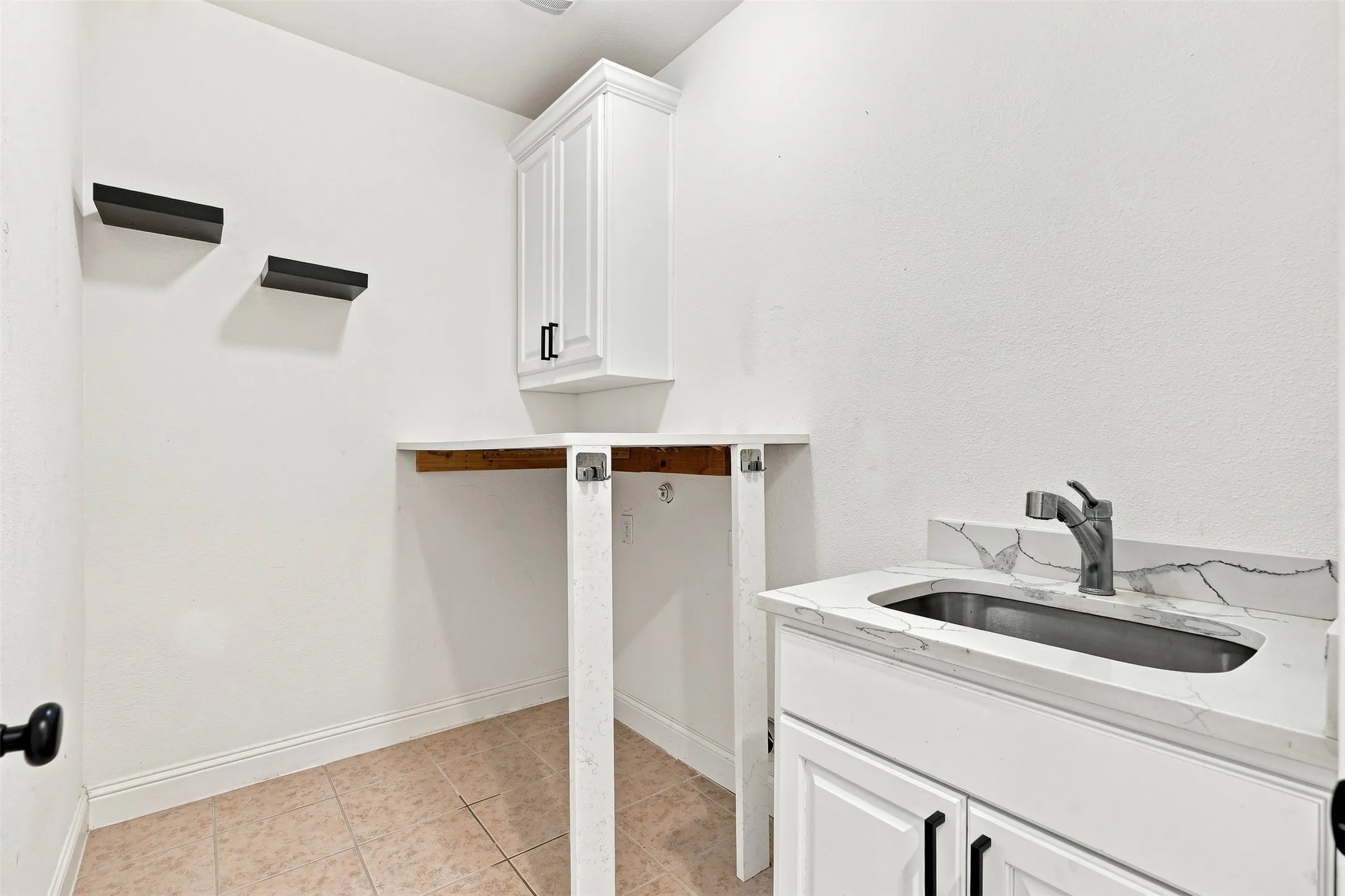 Utility area featuring a white vanity with an integrated rectangular basin, a patterned countertop with a matching backsplash, and a contemporary faucet