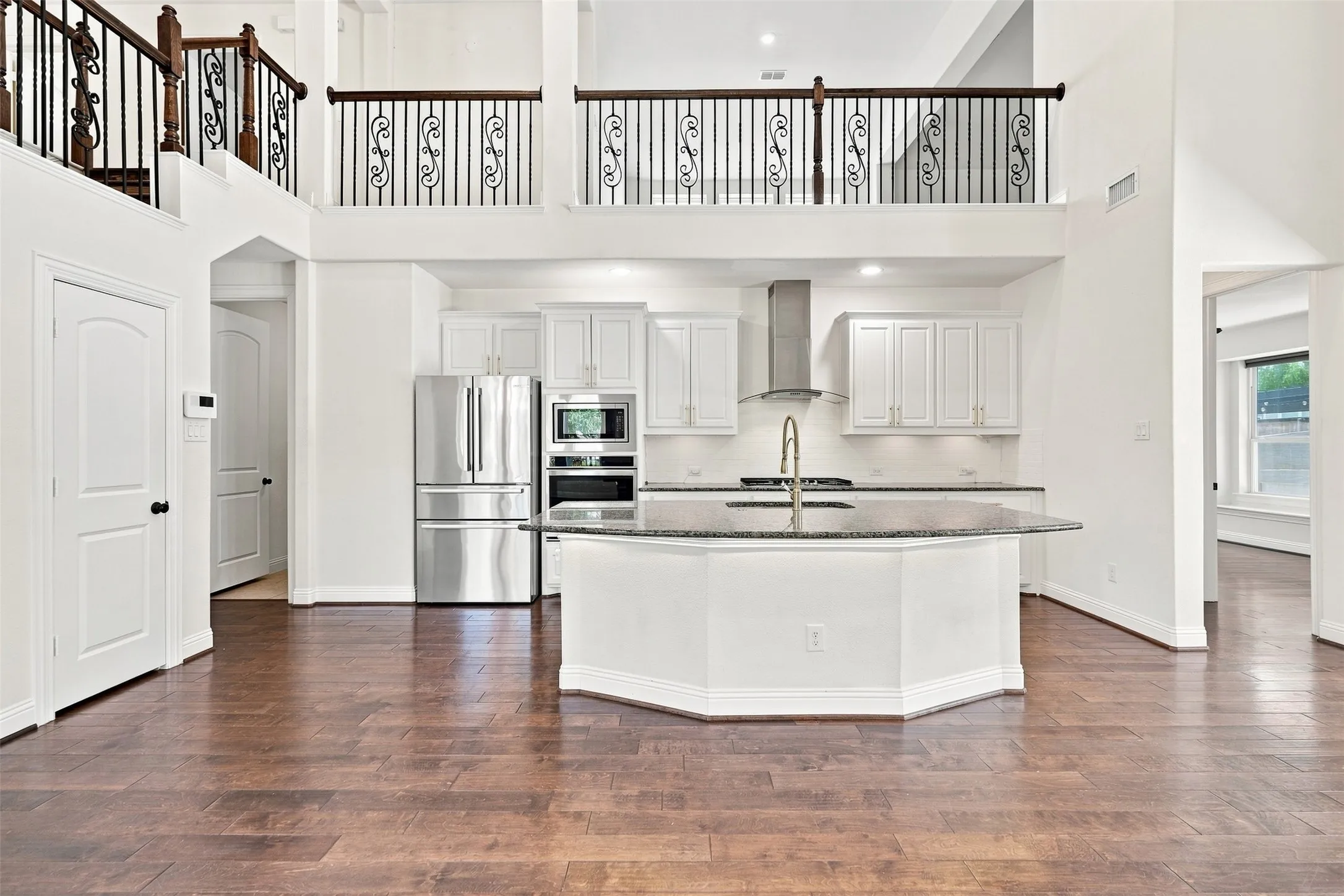 Open-concept kitchen featuring an island with a sink, stainless steel appliances, white cabinetry, and wood-finish flooring