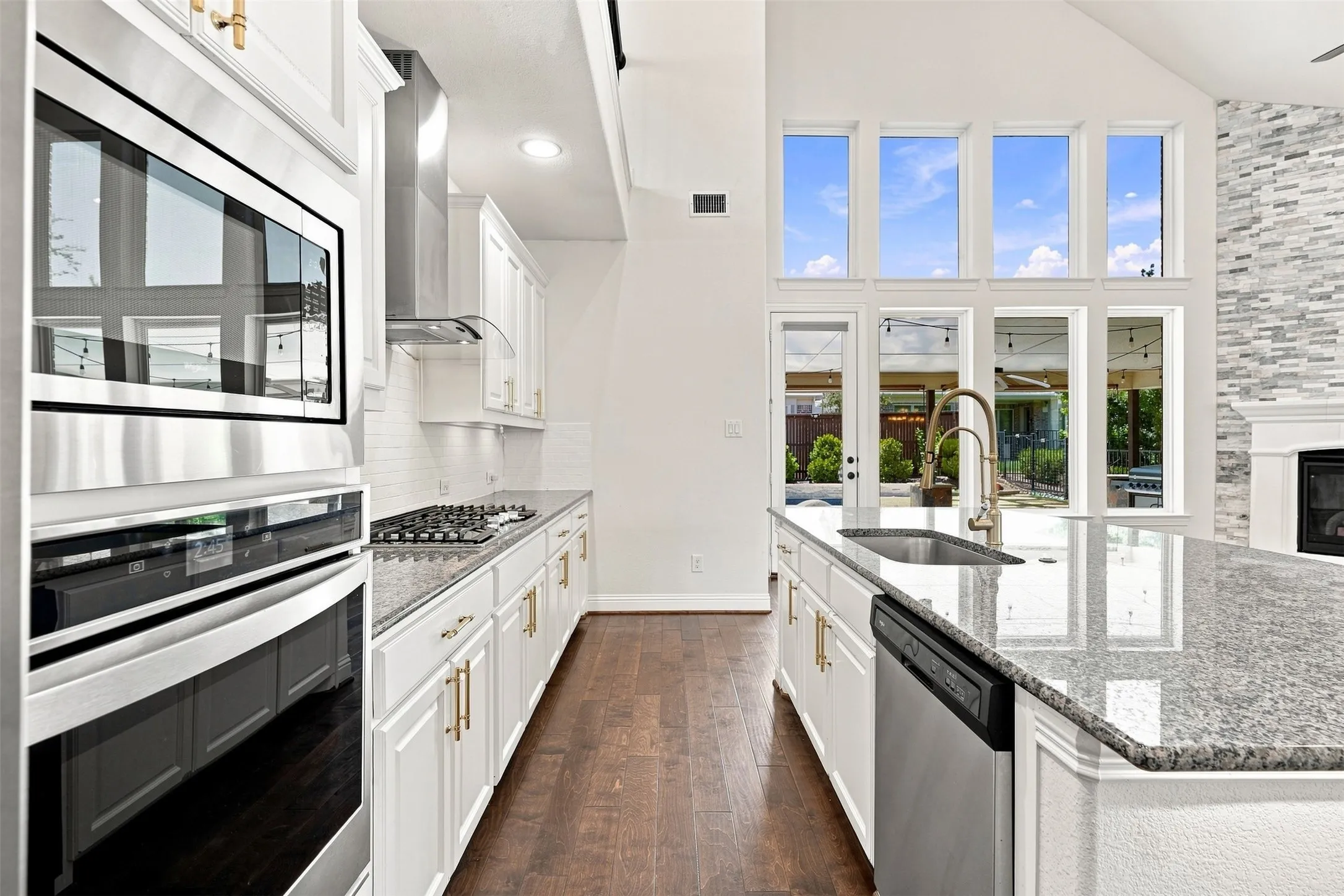 Gourmet kitchen with white cabinetry, granite countertops, stainless steel appliances, wood-finish flooring, and a vaulted ceiling with extensive windows
