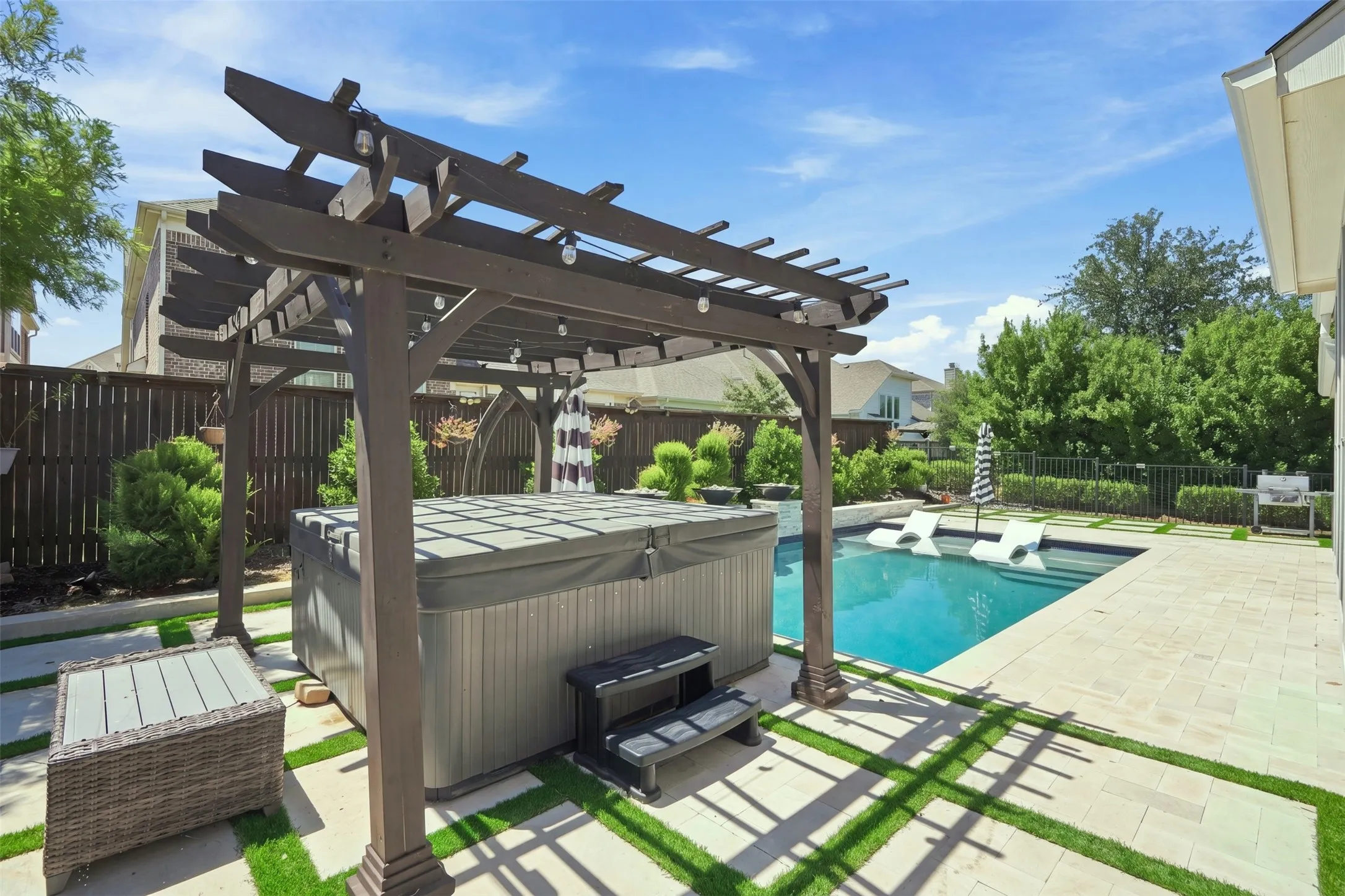 Backyard oasis featuring a swimming pool with integrated tanning ledge, a hot tub under a pergola with string lighting, paver patio, and fenced perimeter