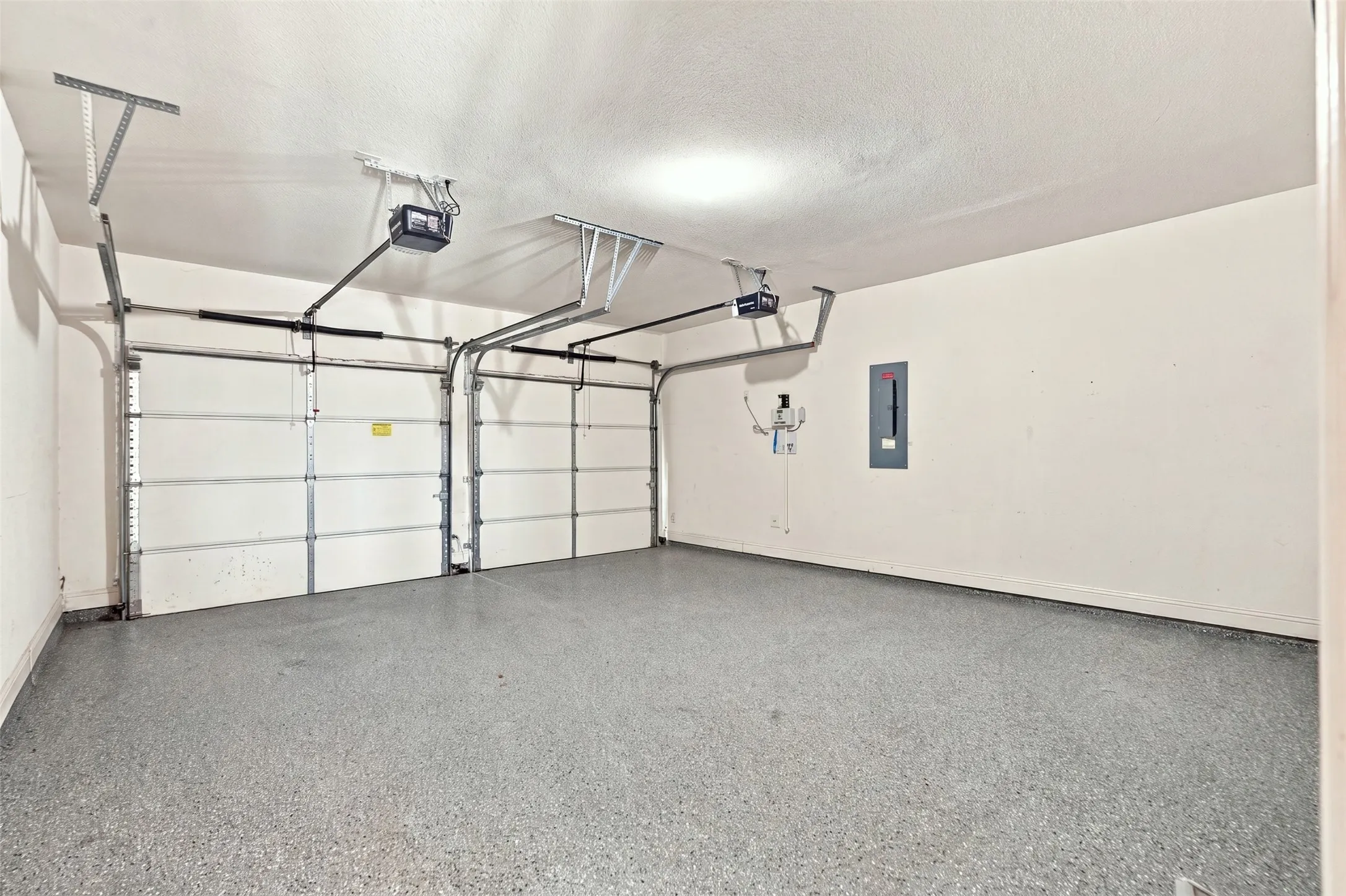 Two-car garage featuring a speckled epoxy floor coating, two overhead garage doors, and two garage door openers