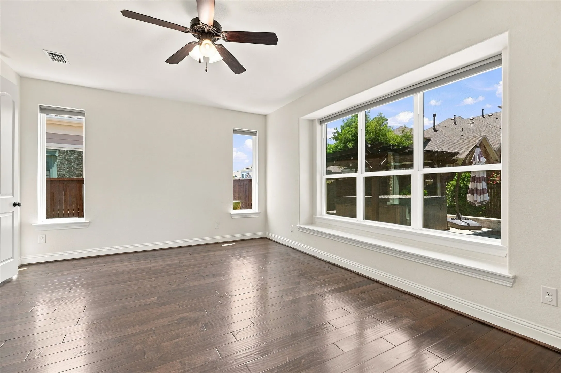 Expansive room featuring wood-finish flooring, a contemporary ceiling fan, and multiple windows