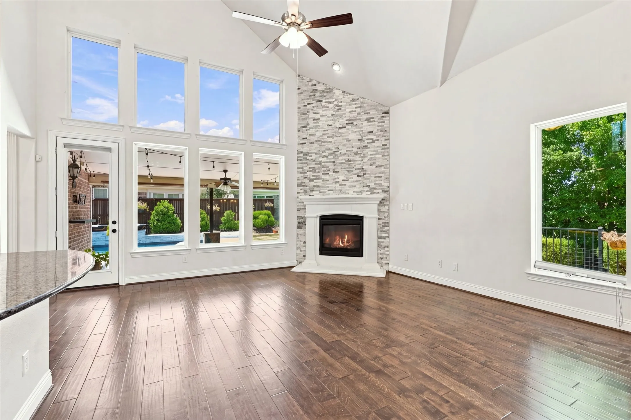 Vaulted ceiling living area featuring wood-finish flooring, a contemporary fireplace with a stone-accented wall, and a full-light glass door opening to an outdoor area with a pool