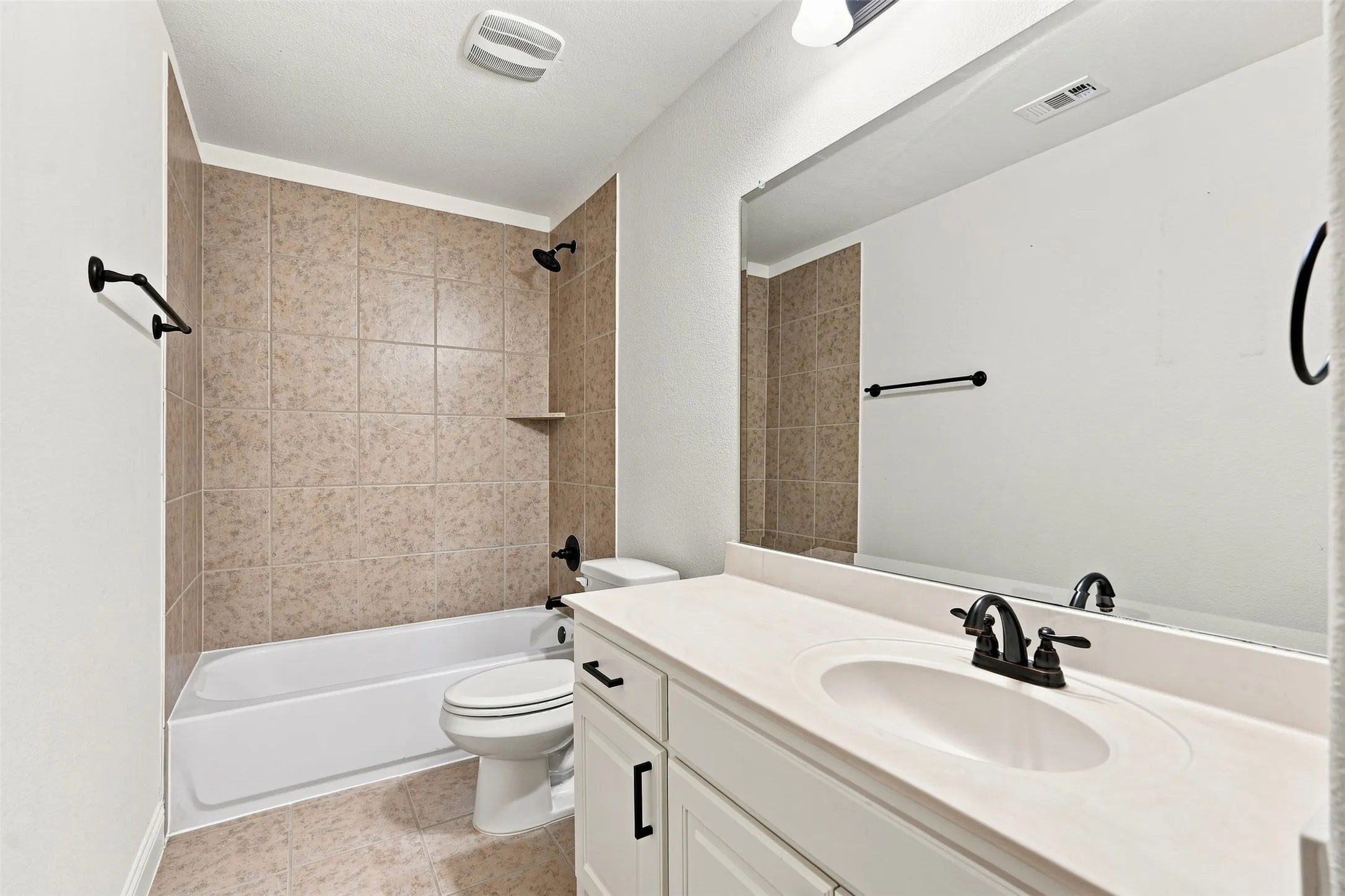 Full bathroom featuring a white vanity with an integrated sink and matte black fixtures, a large mirror, a tiled shower-over-tub combination with a built-in shelf, and a white toilet