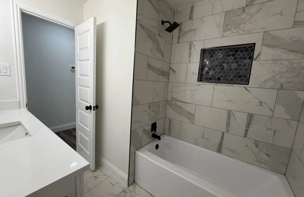 Bathtub with floor-to-ceiling marbled-patterned tile surround, featuring a recessed niche with hexagonal mosaic tile
