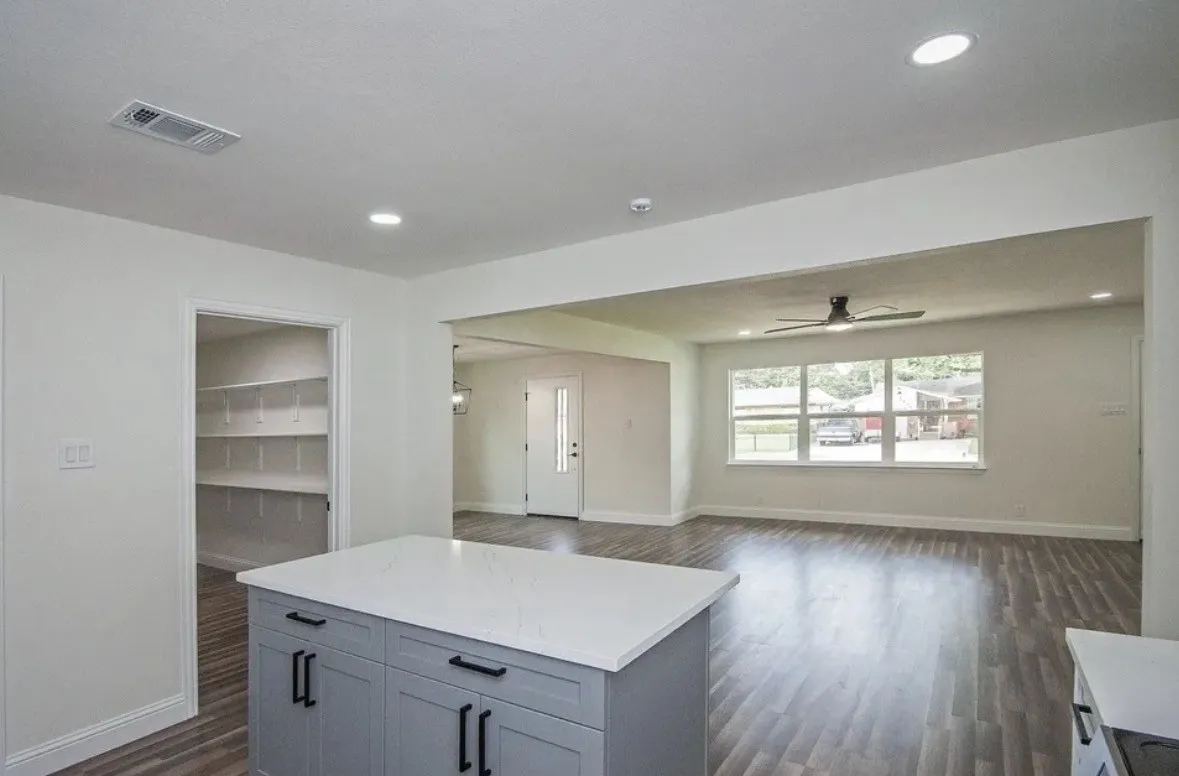 Kitchen island with light gray cabinetry and white countertop, wood-finish flooring, recessed lighting, and a pantry with built-in shelving
